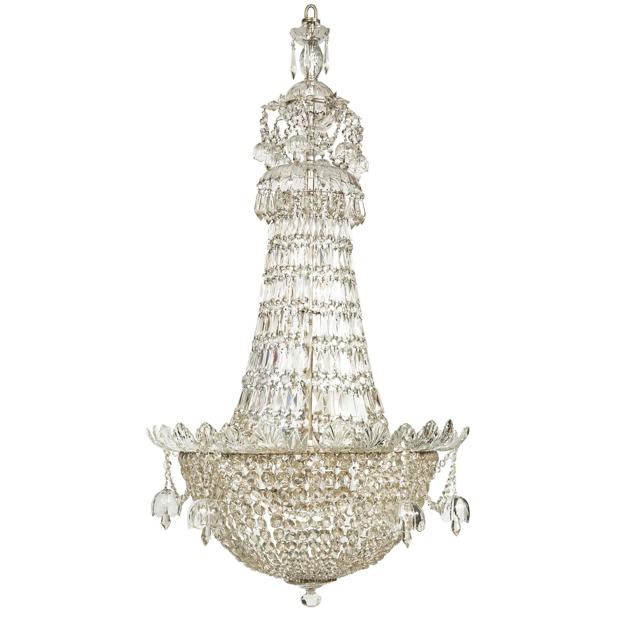 A stunning and very high quality English Louis XVI st. 19th century silvered bronze and Waterford crystal twelve light chandelier. The chandelier with a bottom dome with octagon shaped cut crystal garlands lead to a central band of crystal