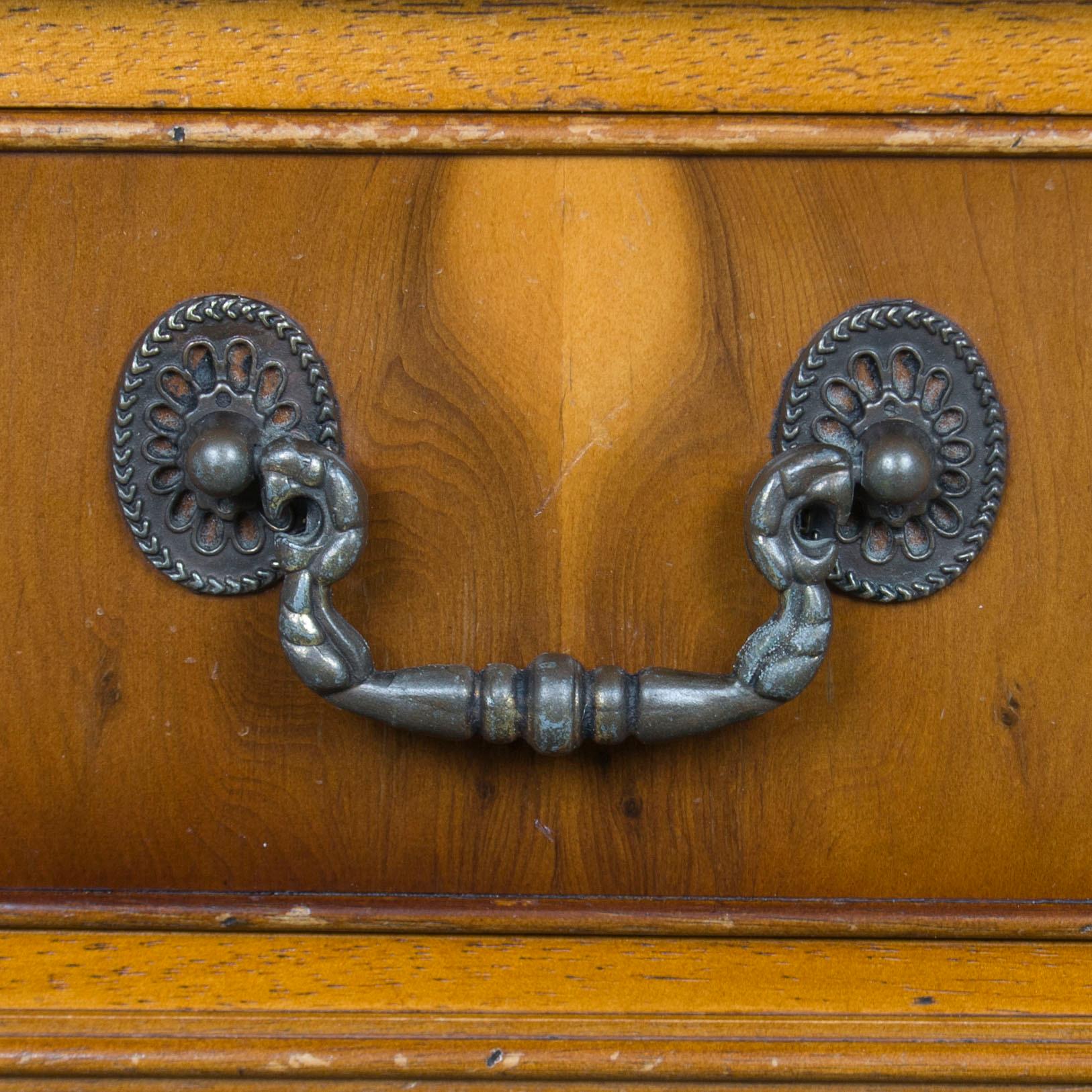 This antique style yew wood bookcase was crafted in England, circa 1960. Today, the bookcase remains very sturdy and quite beautiful. The drawer fronts are adorned with brass swan neck pulls. Yew cross banding and black ebony string inlay adorns the