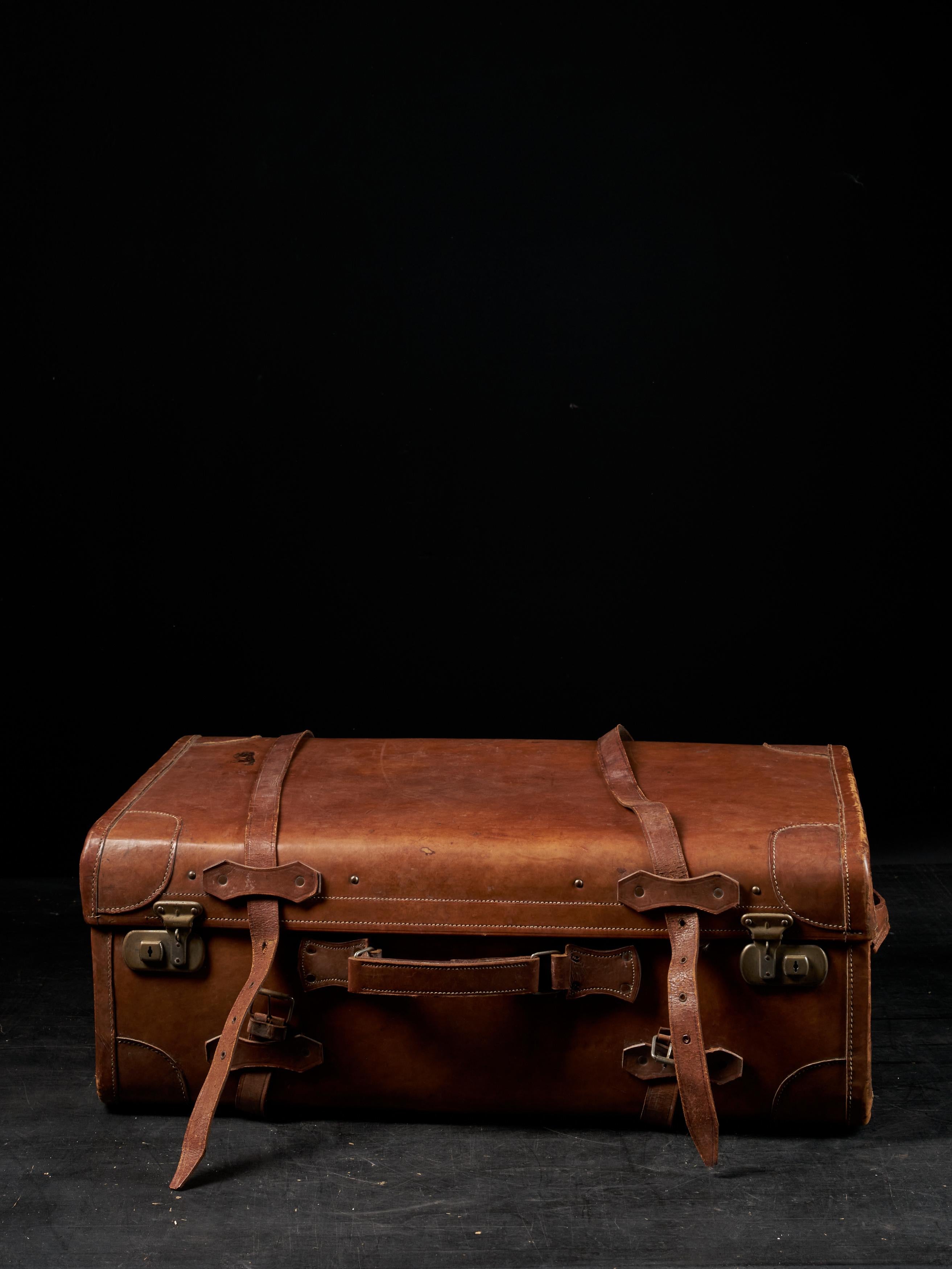 A simple leather suitcase with luxurious details. On the clasp ‘ENGLAND MENE’ is engraved. The inside is finished with quilted blush pink fabric and a small side pocket with rushing at the top. Two leather buckles that go around the whole suitcase,