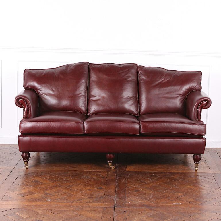 English three-seat Oxblood leather sofa on turned mahogany bun feet with brass castors. Exceptionally comfortable sofa, the leather in excellent condition. English-made.

Measures: 78? wide x 36? deep x 38? tall x 20? seat height.

