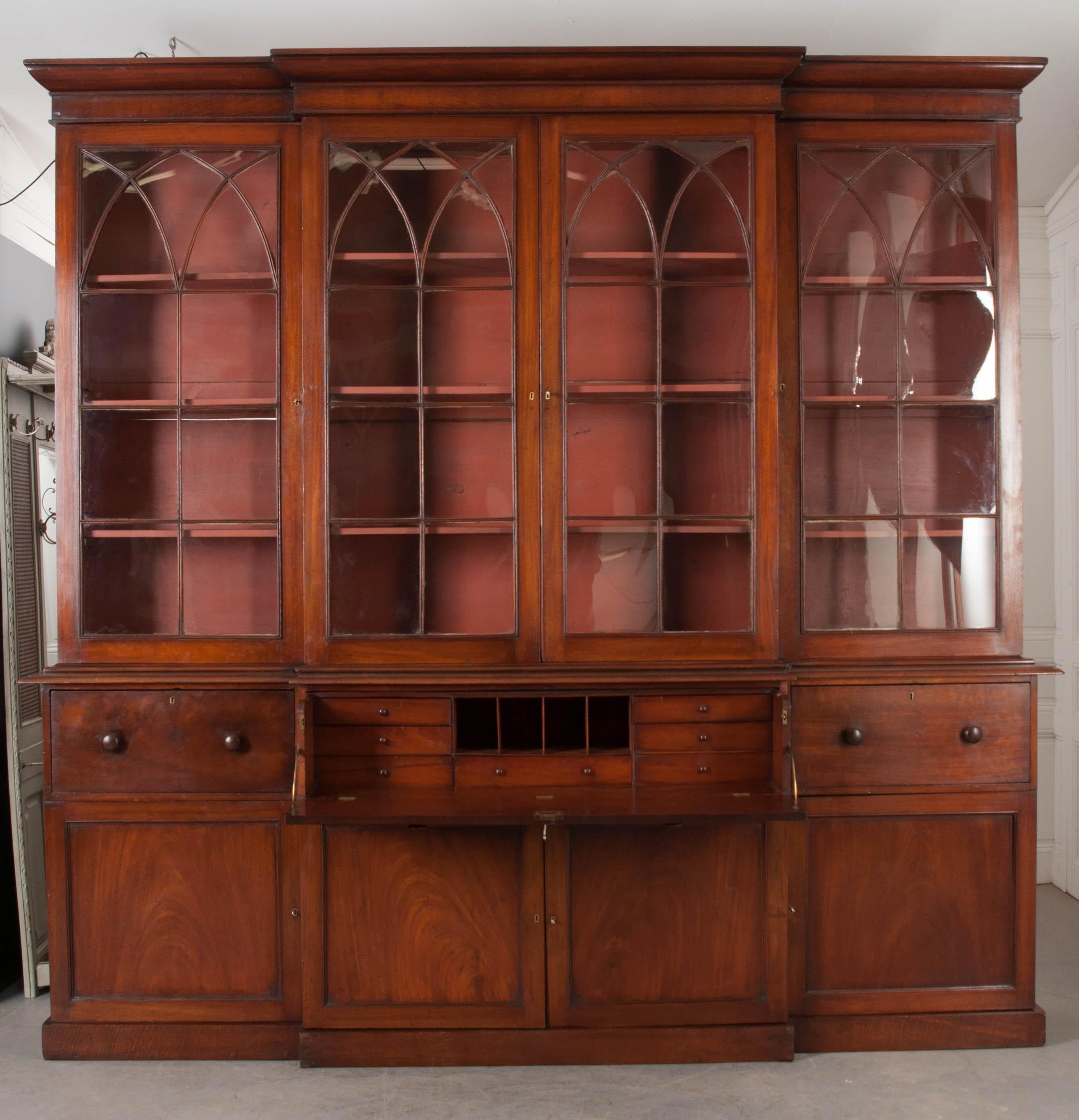 An incredible breakfront bookcase, made of mahogany in the Georgian style, with incorporated desk. Made circa 1810, this stunning English piece has three glass-front upper cabinets set above a cased plinth base. The upper cabinets have all of their