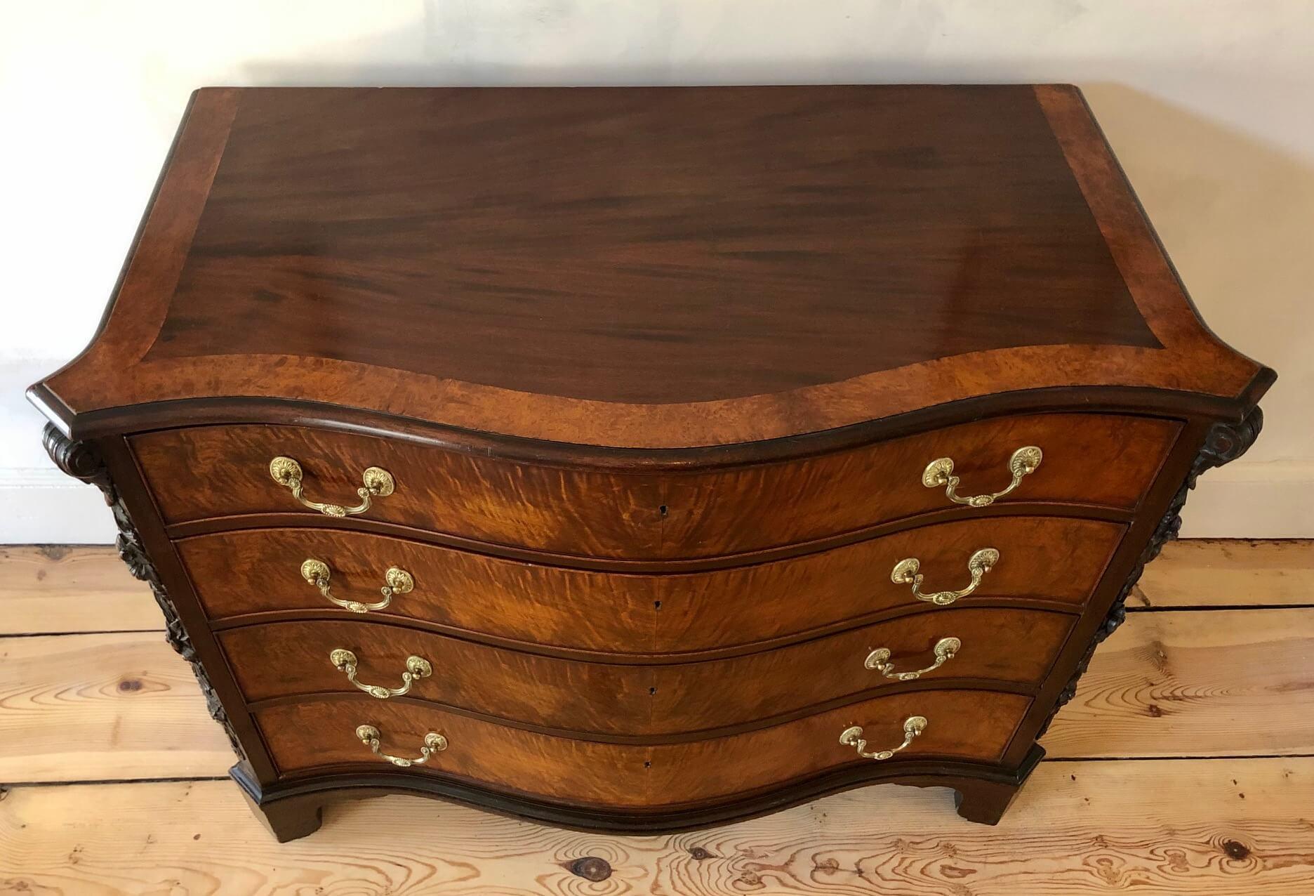 Fine and authentic English bench made solid mahogany serpentine front chest of four drawers after a design by Thomas Chippendale (1718-1779) of circa 1755; the top with burled amboyna border above canted corners with elaborate hand carved acanthus