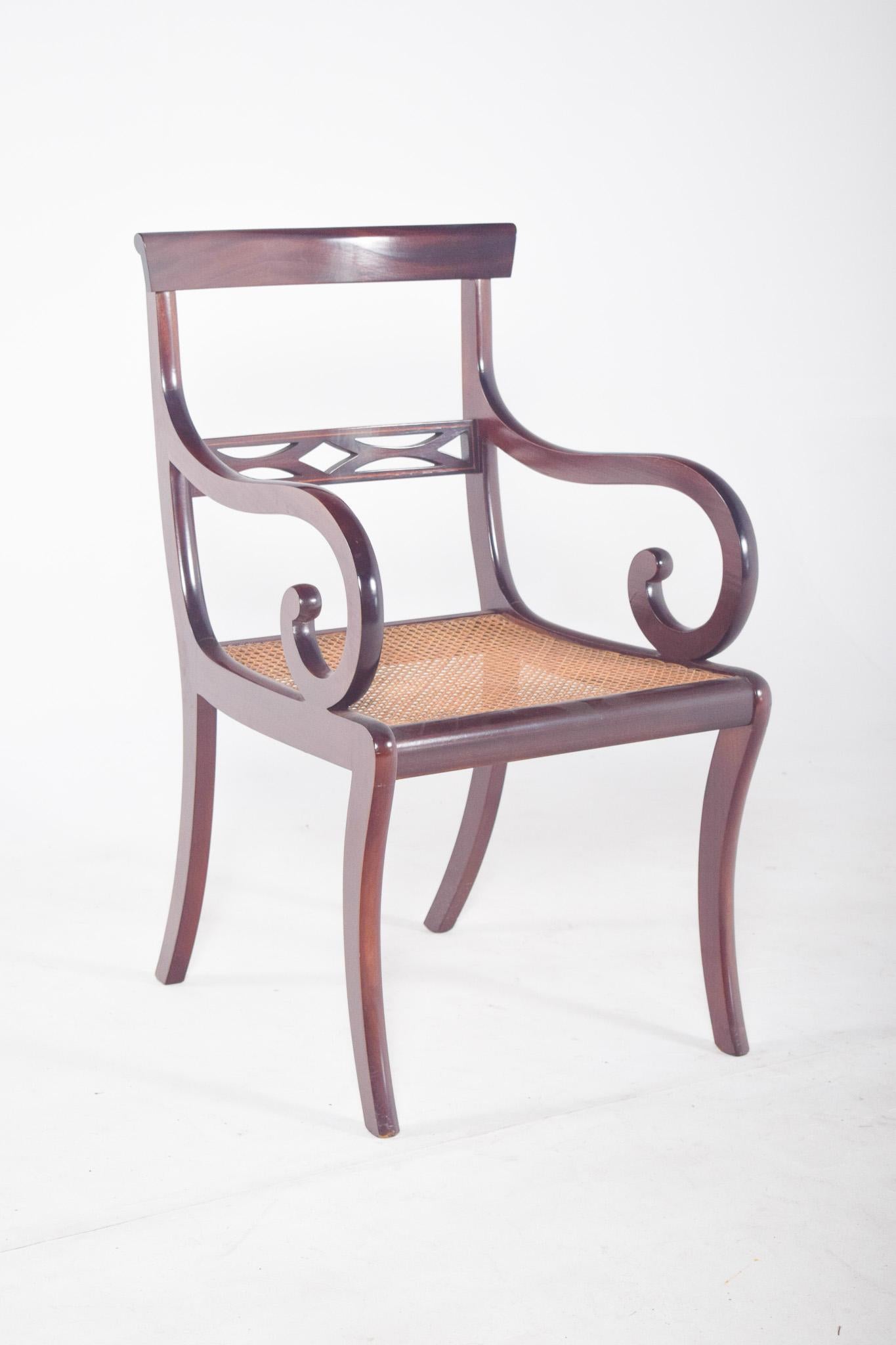 Chaise en acajou avec assise en paille.  Les jambes sont incurvées, l'arrière est légèrement arqué et l'avant est en forme de sabre. Les bras, également incurvés, se terminent par une boucle décorative. Le dossier est bas, avec une traverse