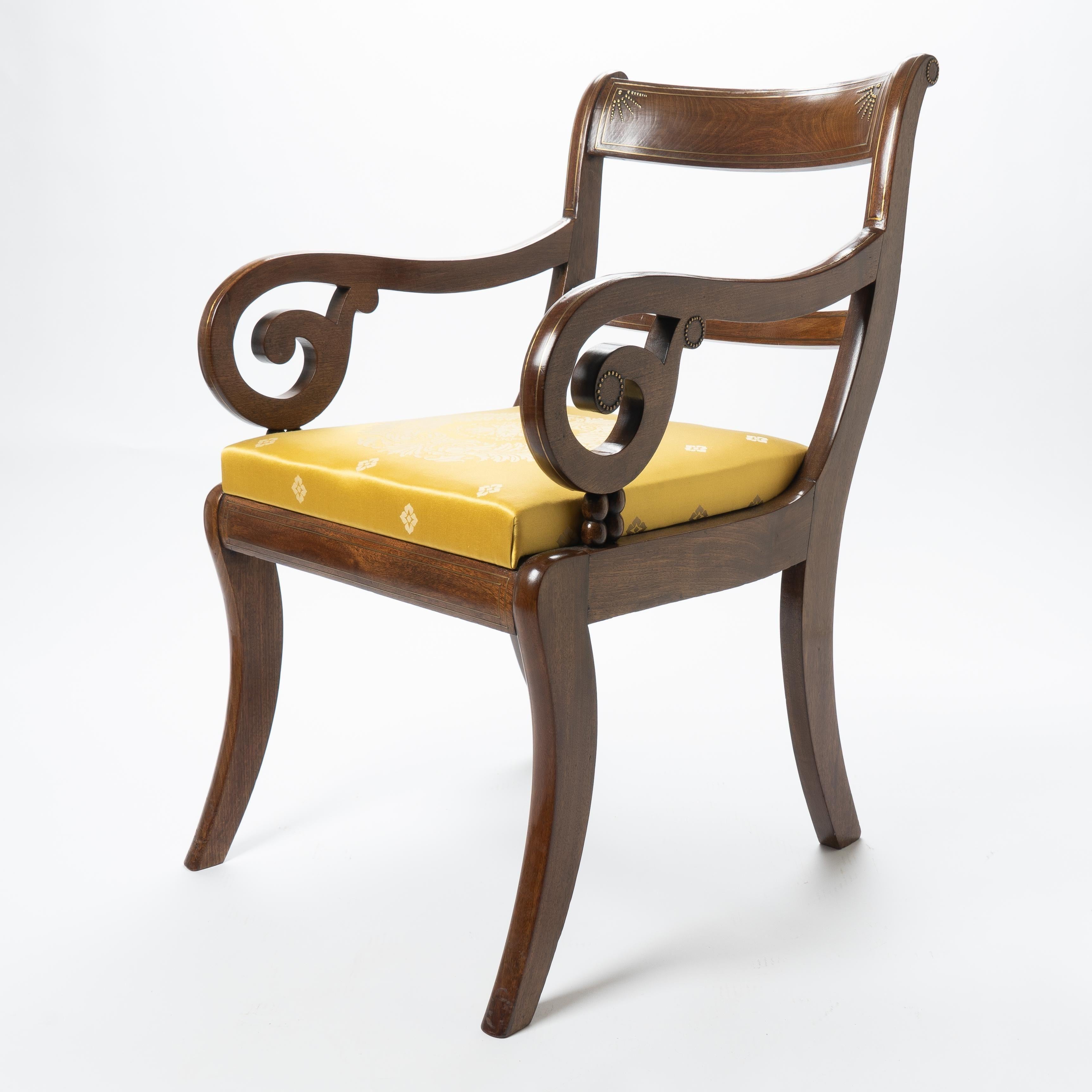 English Regency period ram’s horn arm chair on sabre legs. The chair back has a rectangular concave crest rail morticed between the upper leg posts and over a horizontal back rail. The construction is of solid mahogany with decorative brass string