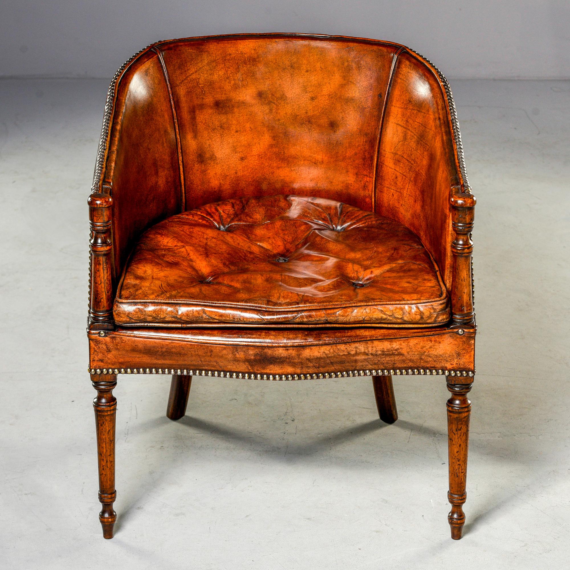 Leather and mahogany barrel back chair, circa 1930s. Original leather upholstery with removable tufted seat cushion, brass head upholstery nails. Mahogany frame features turned front legs and arm supports. Unknown maker. Leather shows wear/age but
