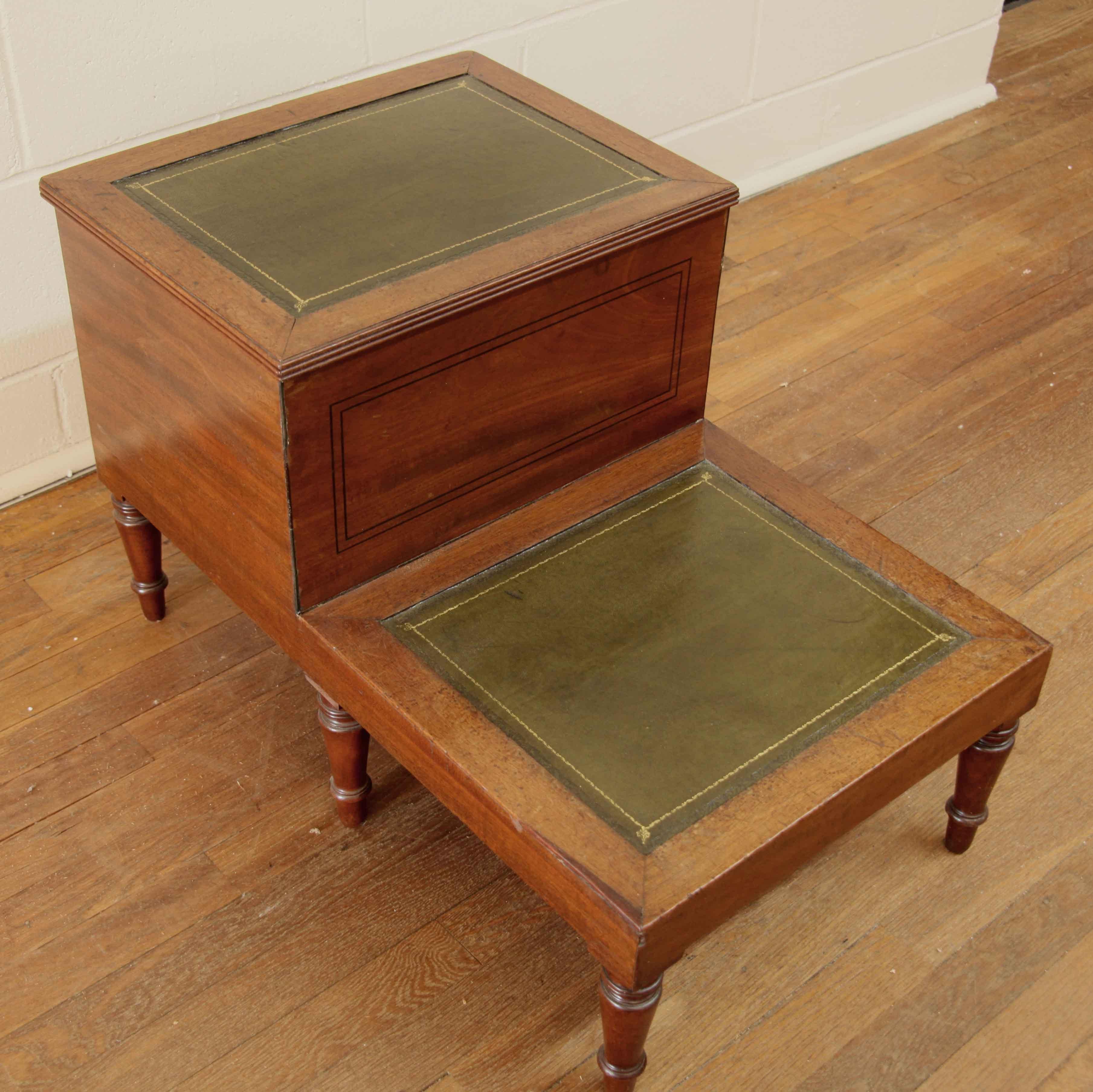 English mahogany bed steps,  the upper step lifts and has open storage below.  The front is veneered with swirl grain mahogany and is inlaid with ebony .  The two steps are covered with gold tooled green leather.  The piece rests on turned feet.   