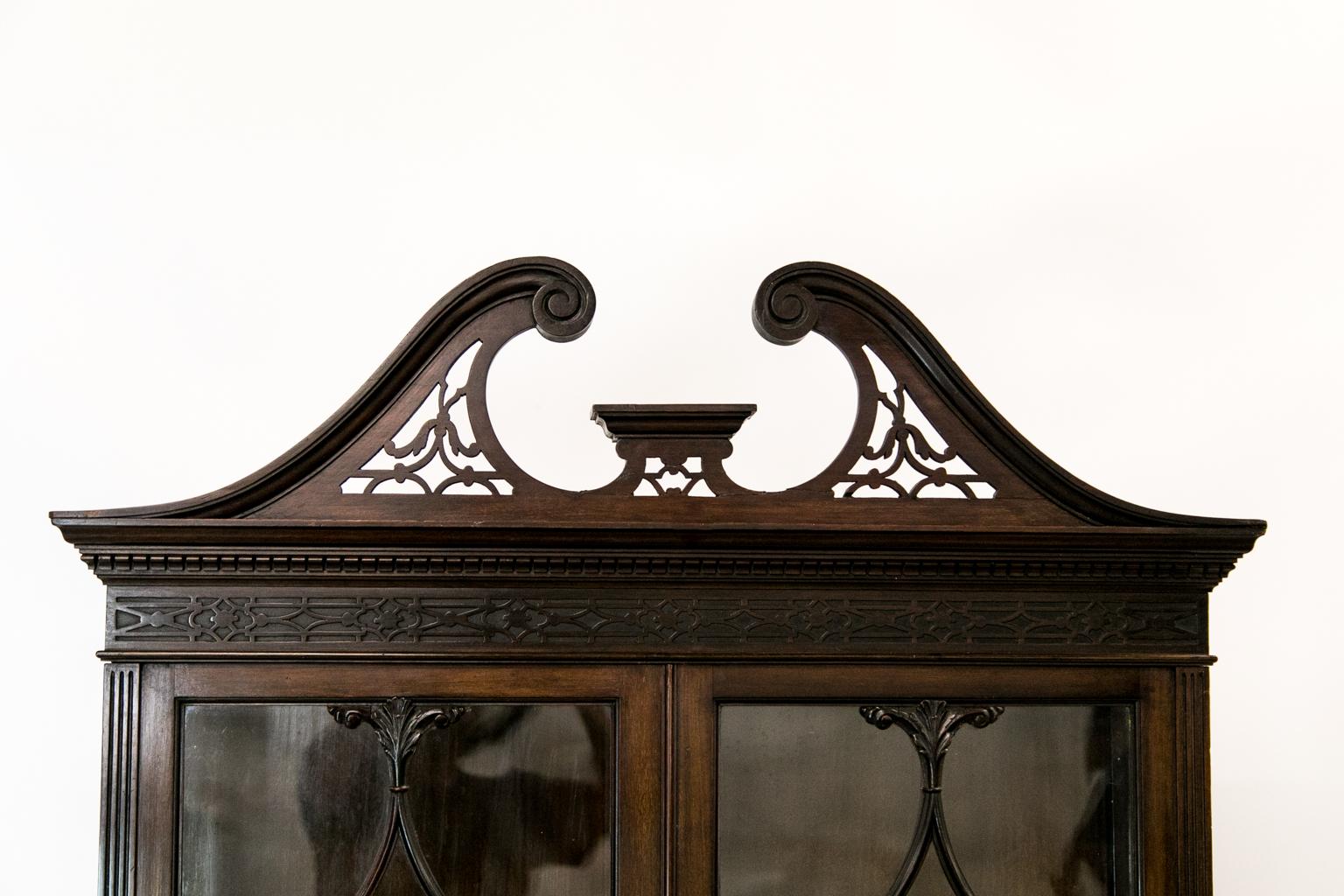 The upper display cabinet of this mahogany bookcase on stand has the original wavy glass doors. The side stiles of the drawers are fluted and the frieze has blind fretwork. The crown molding has ogee shaped dentil work. The top has a broken arch