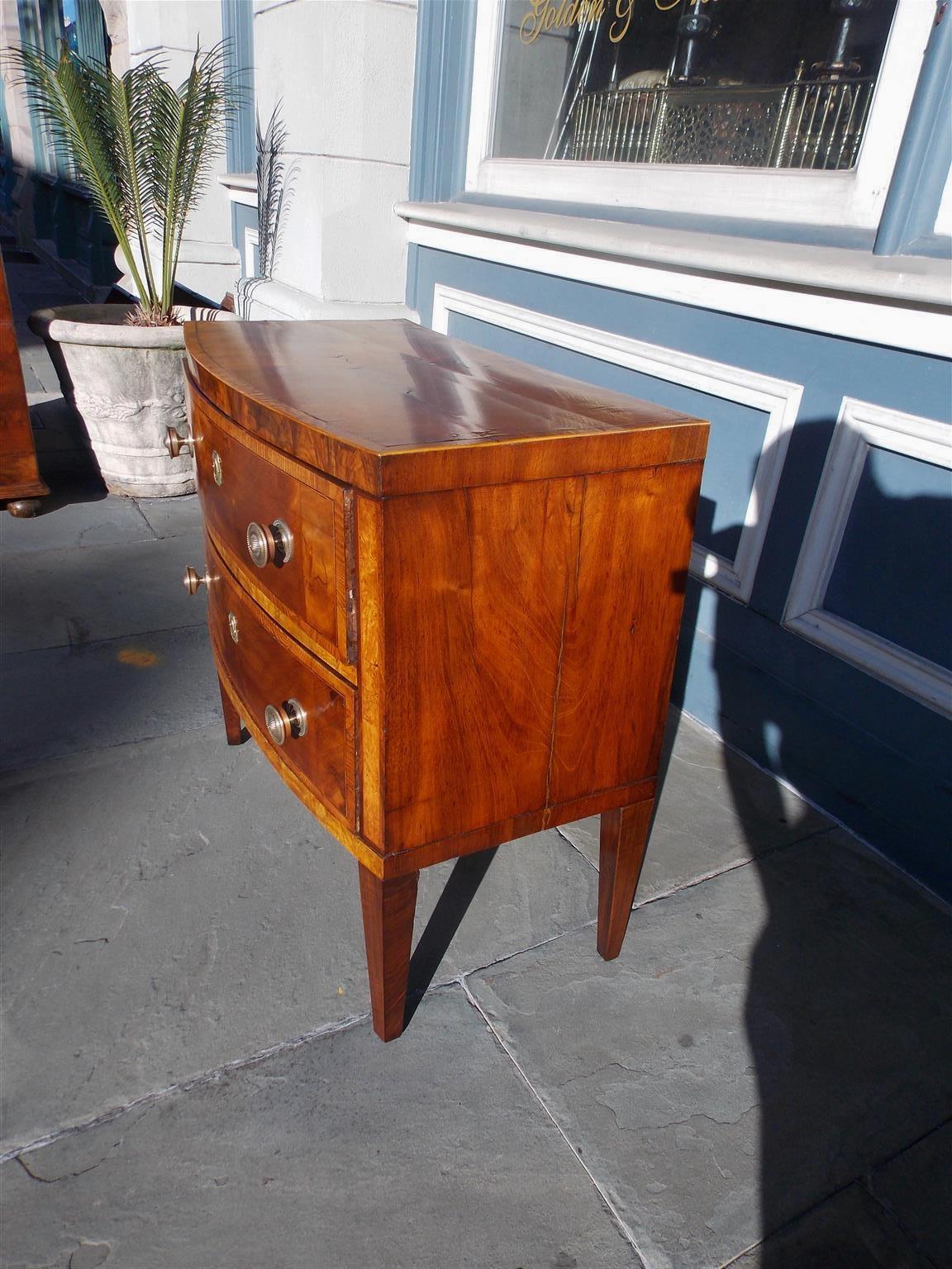 English mahogany bow front two drawer chest with satinwood cross banded inlays, original brasses with escutcheons, interior locks, and resting on the original squared tapered legs. Late 18th Century.