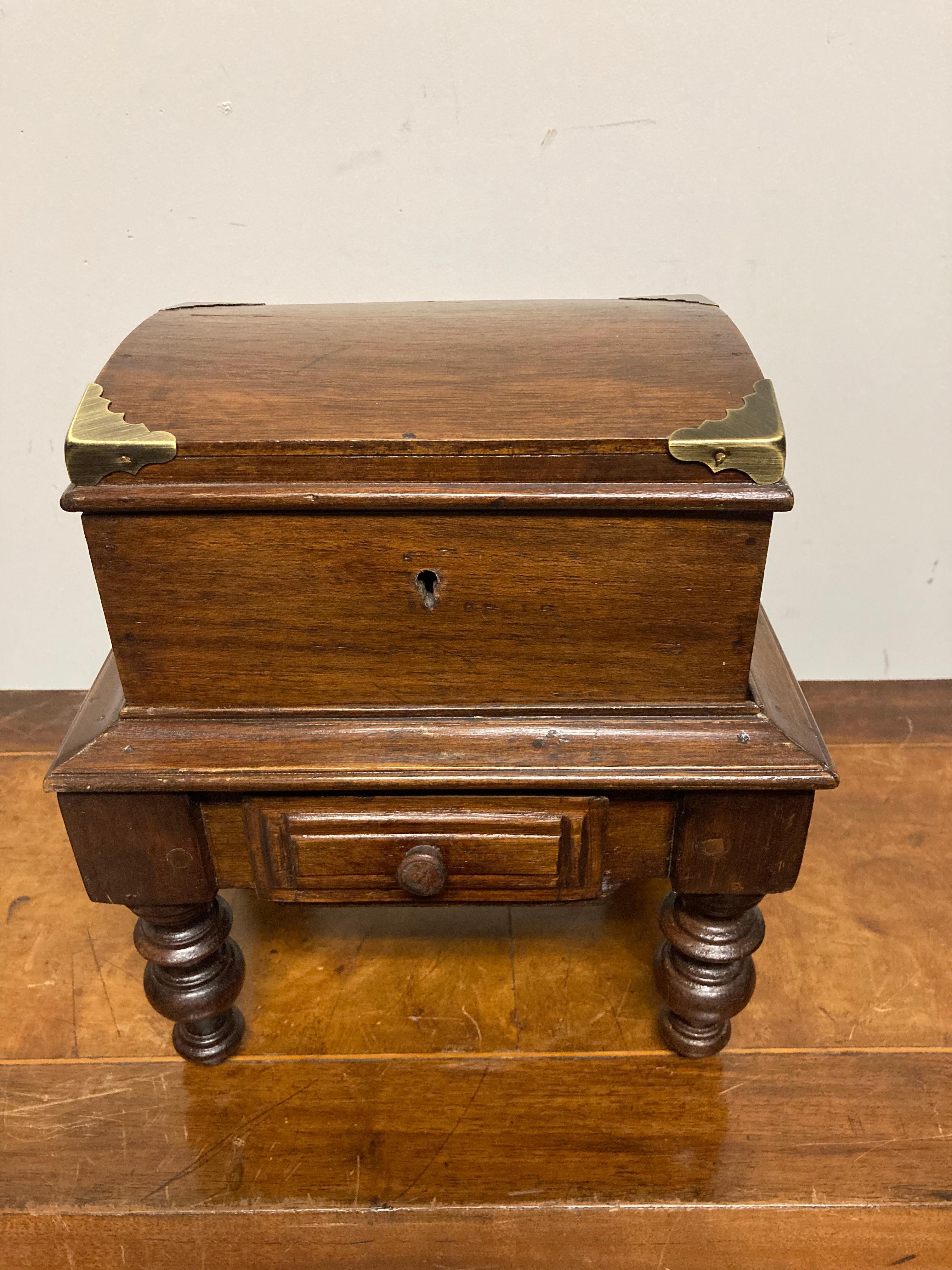 A sweet little box on stand from the Edwardian period. The box, likely originally a tea caddy, with brass corners. The base with turned legs and a single drawer. The box lifts out of the base. 
Measures: 10.75 inches high 9.5 wide 7 deep.