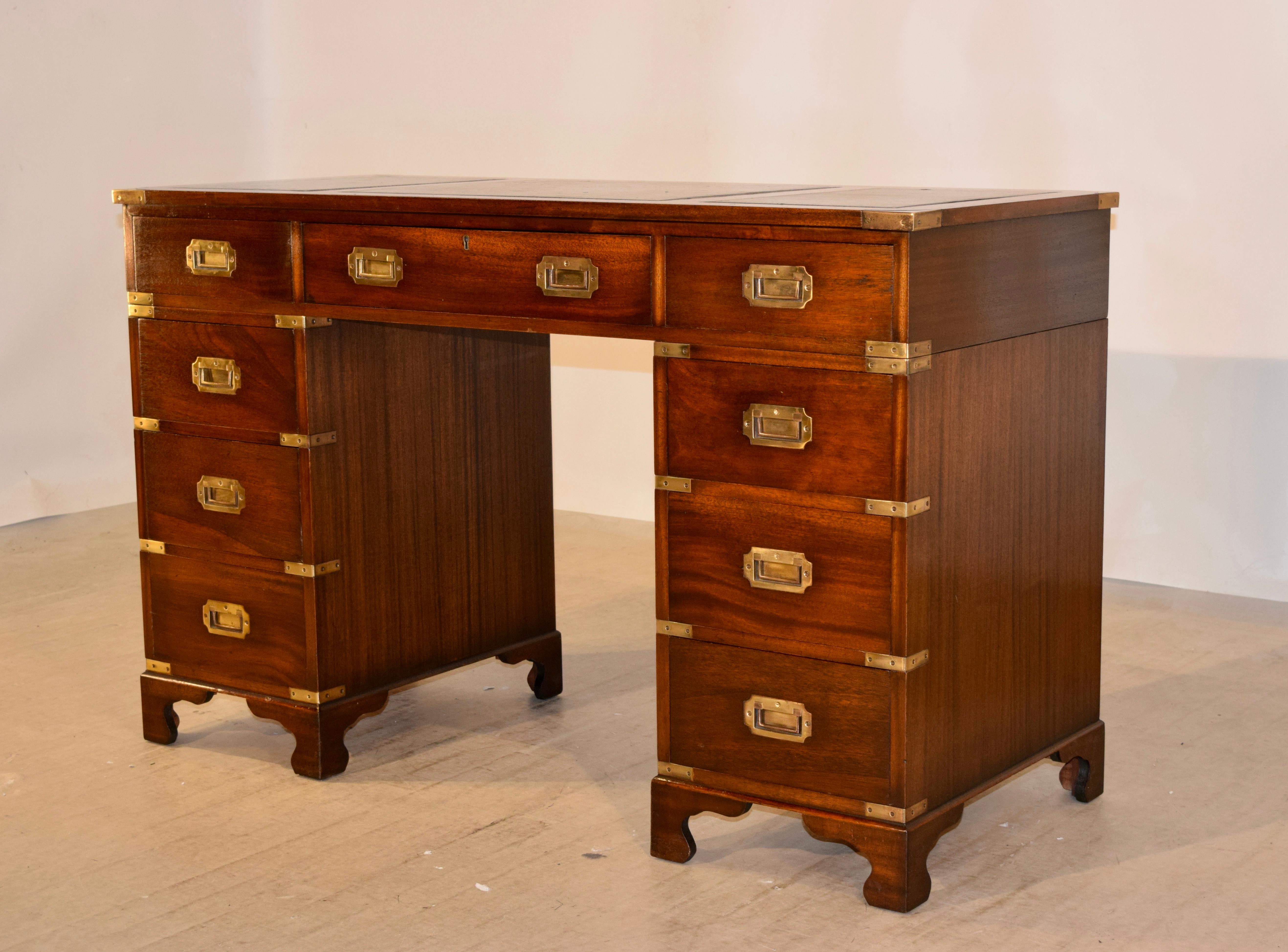 Campaign style desk from England and made from Mahogany, circa 1940-1950. The top has three panels which are covered in lovely green leather with gold tooling and surrounded by mahogany borders, following down to three drawers. The top is supported