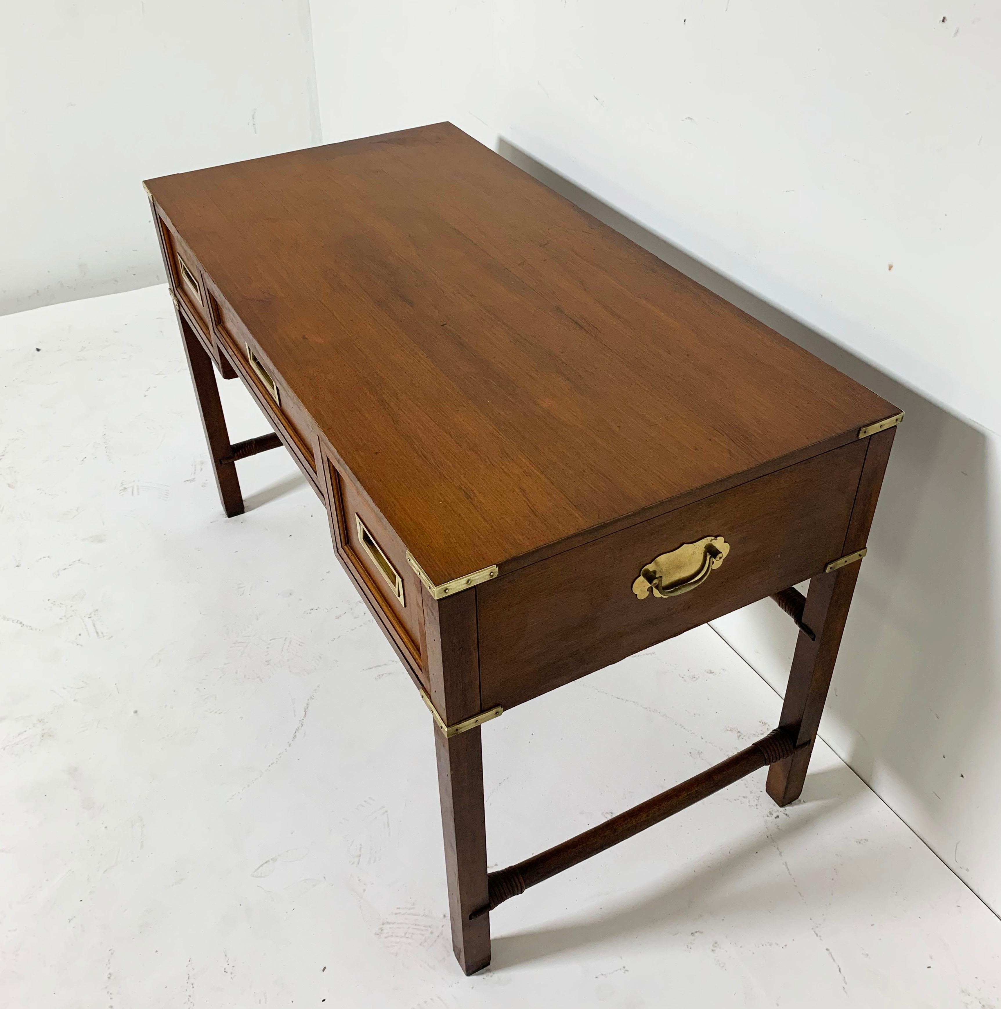 English mahogany writing desk with side lift handles in the campaign style, circa 1960s. Cane wrapped accents on the stretchers and brass sabots on all legs.