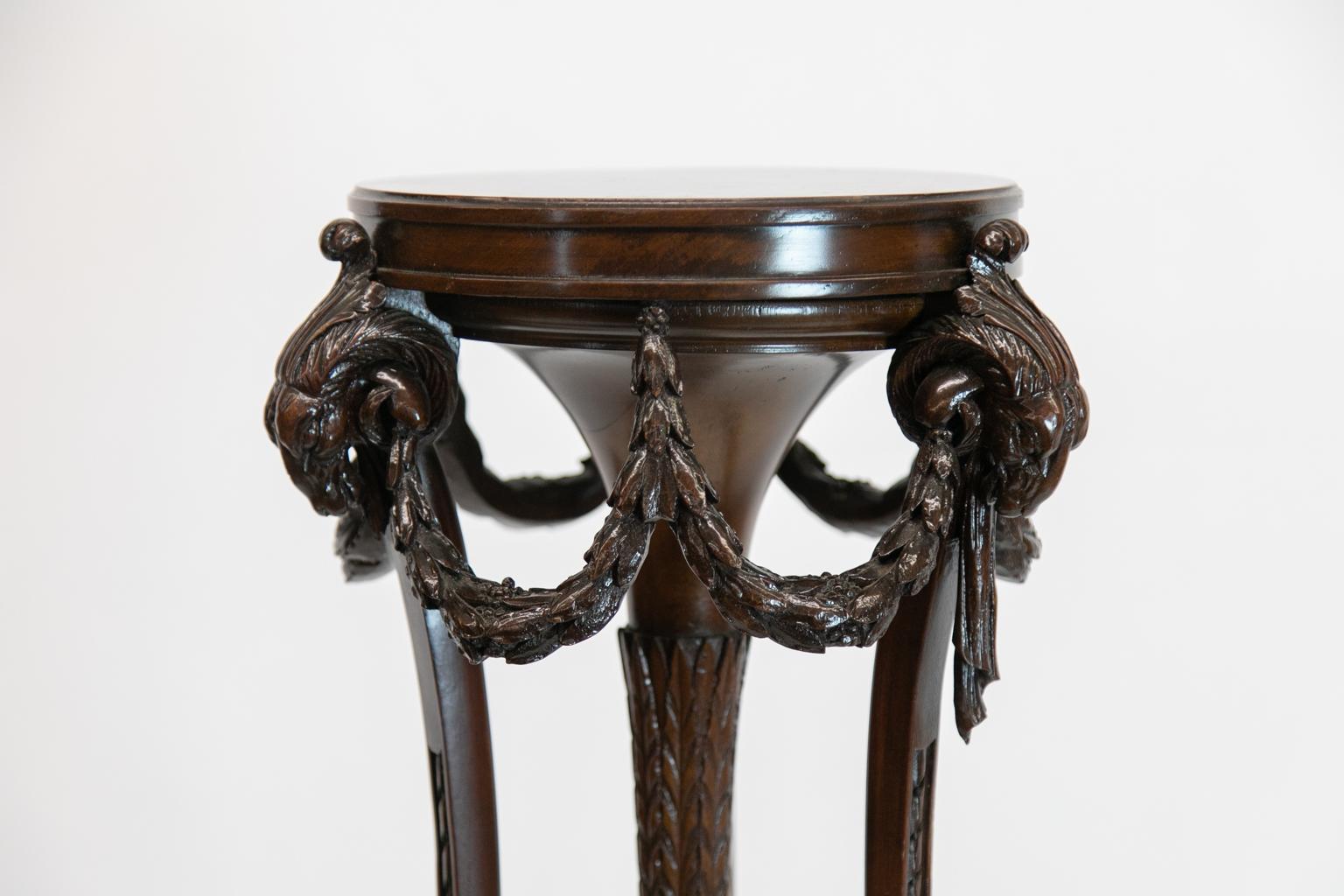 English mahogany carved fern stand is carved with stylized horse heads and draped with foliate swags. There is a central descending pendant carved with stylized acanthus leaves. The legs are carved repeating ribbon terminating in carved hoof feet.