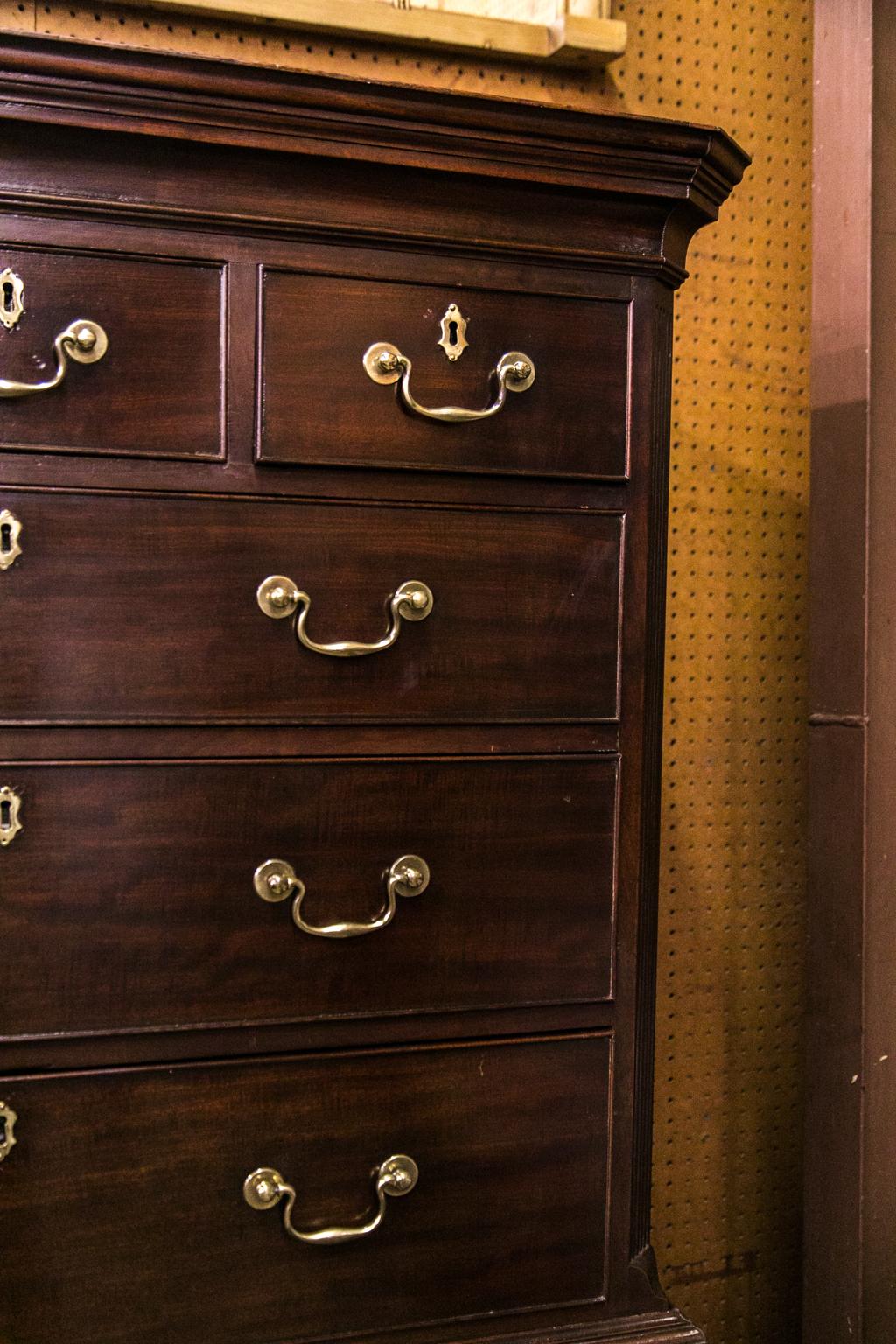 This 18th century chest retains its original hardware, ogee feet, and crown moldings. The upper section has fluted chamfered corners that terminate in lamb's tongues at the base. The lower section has a pull-out brushing slide. The hardware has been