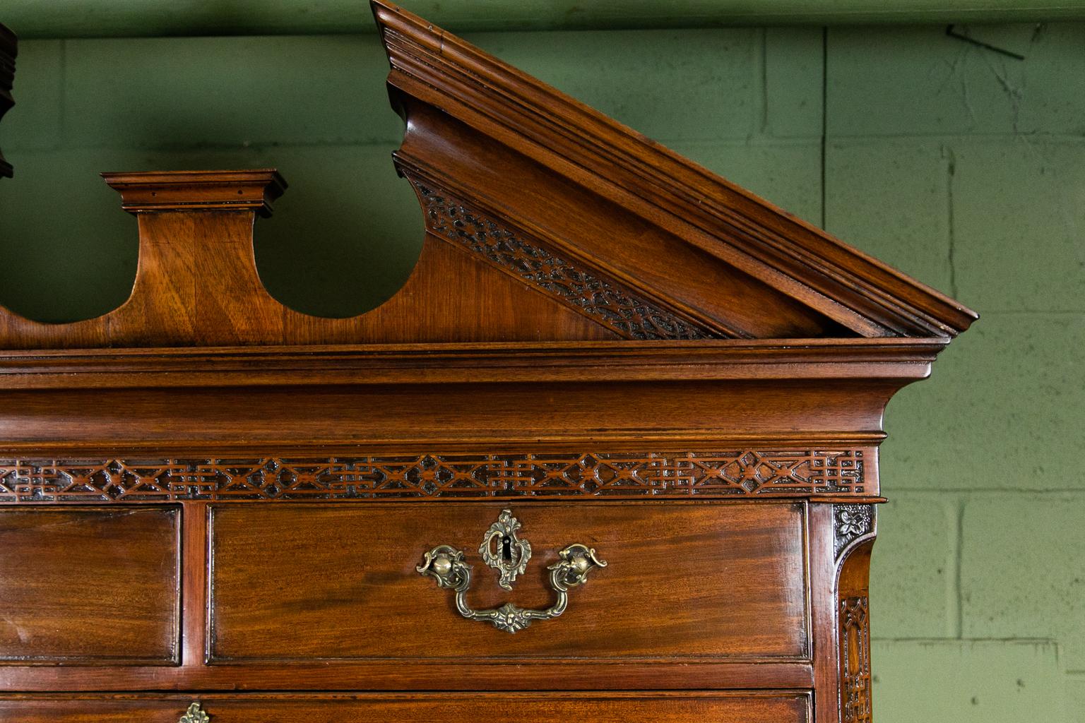 English mahogany Chippendale chest on chest has the original Rococo hardware. It has Fine fretwork in the frieze and the broken arch pediment. The blind fretwork extends to the sides and on the base of the upper section. The chamfered corners also