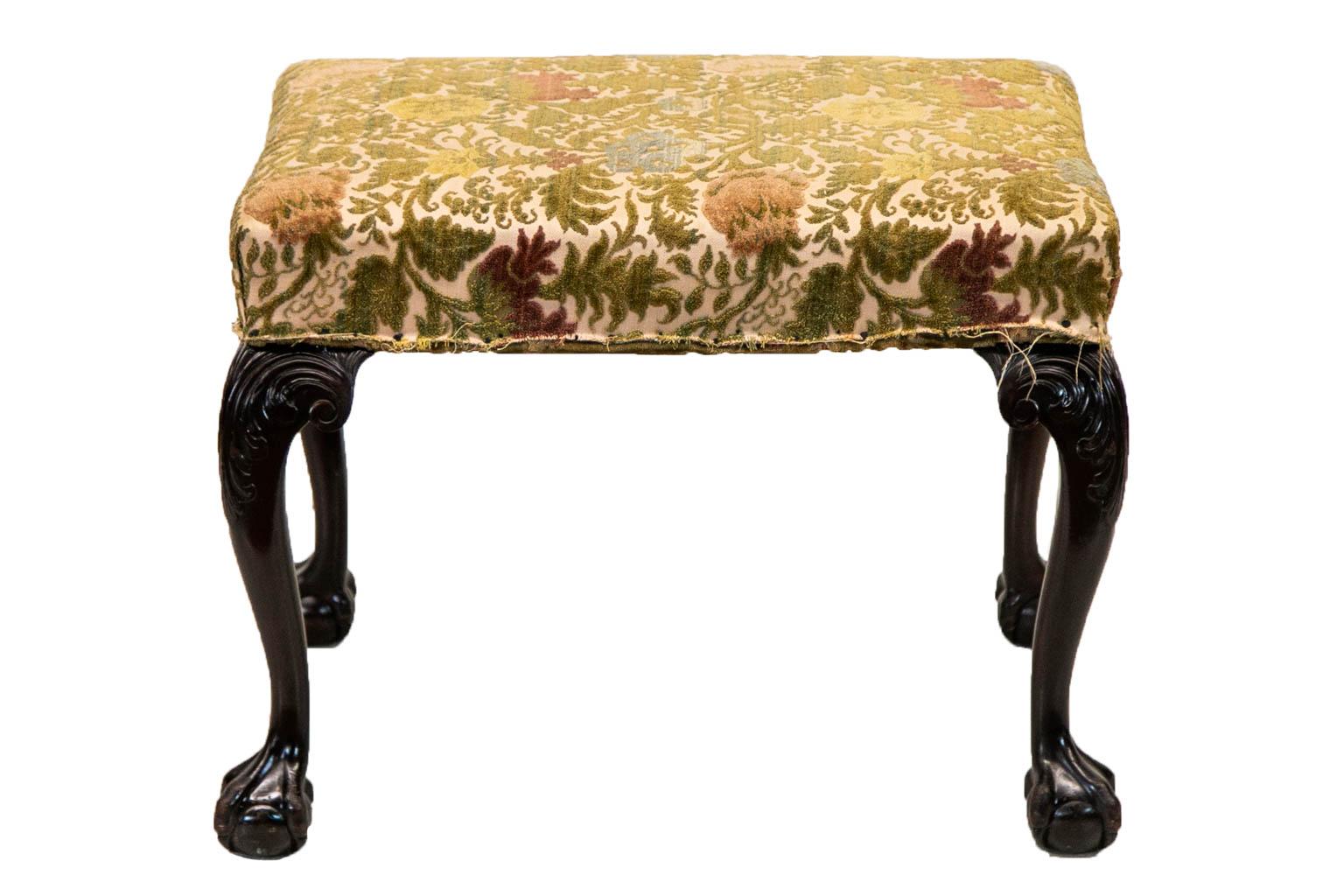 The cabriole legs of this stool are carved with acanthus leaves on the knees. The legs terminate in claw and ball feet. The upholstery is similar to crewel work and has some wear but is serviceable. There is no gimp edging.