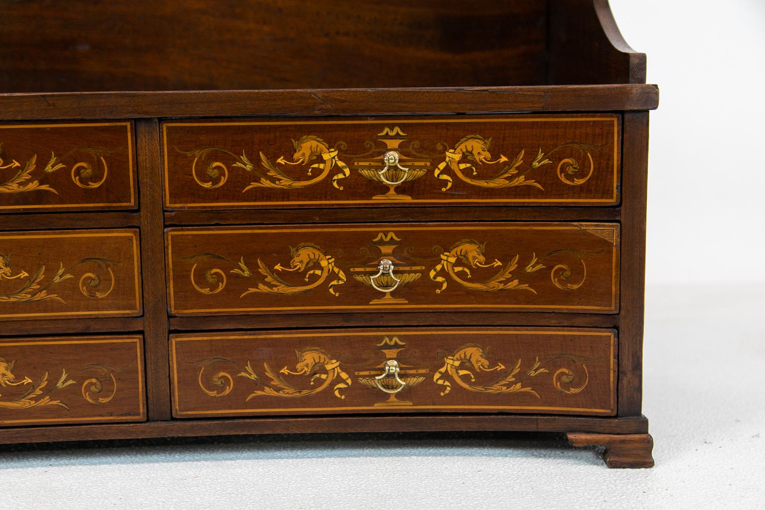 English mahogany concave inlaid countertop chest with the drawers inlaid with boxwood, satinwood, and engraved classical urns and dragons on ogee feet.
