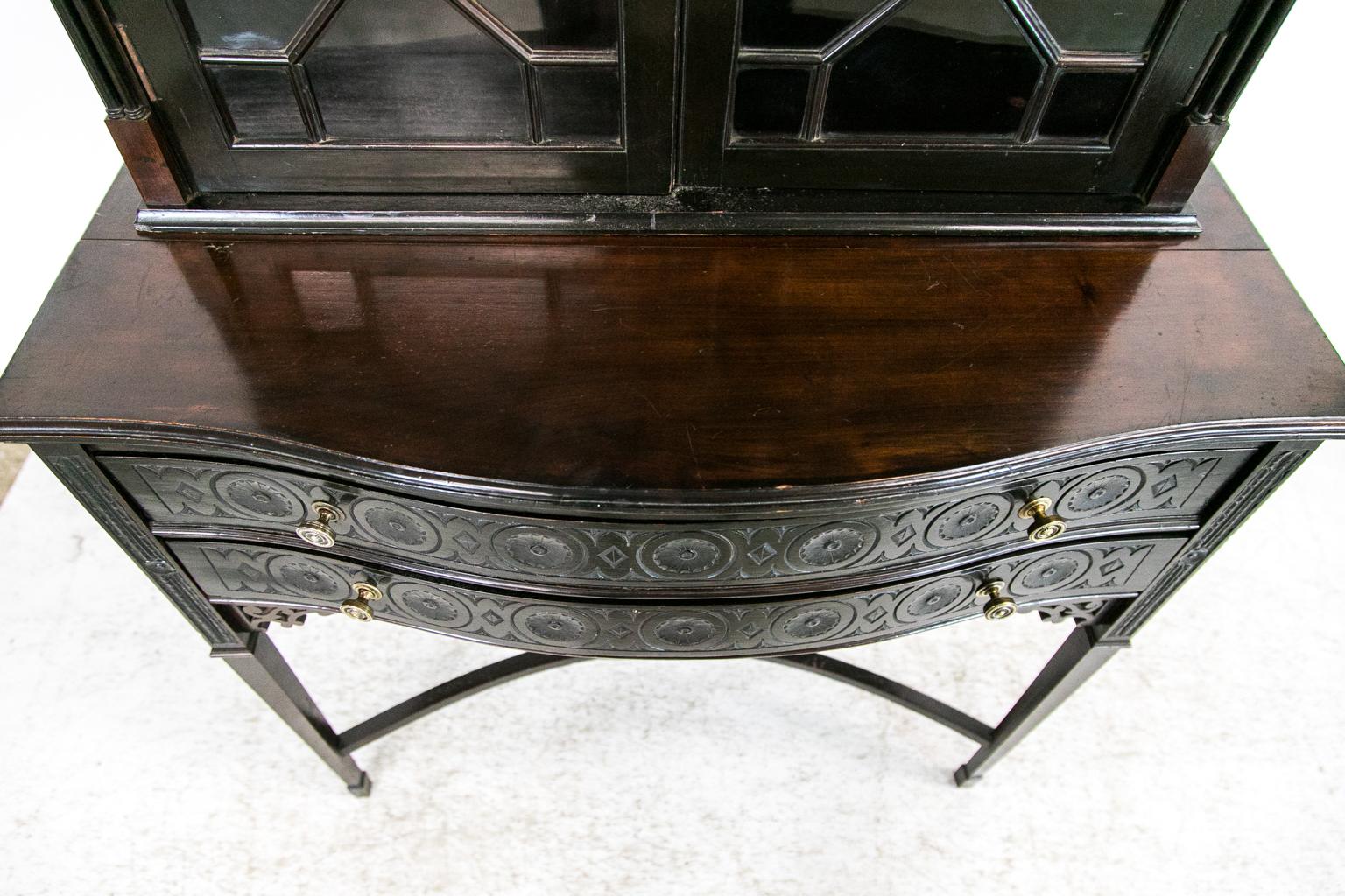 The top half of this display cabinet/bookcase has a broken arch pediment with open fretwork carving. The frieze is carved with repeating arches and the stiles have two double free standing small columns. The lower section has a serpentine shape and
