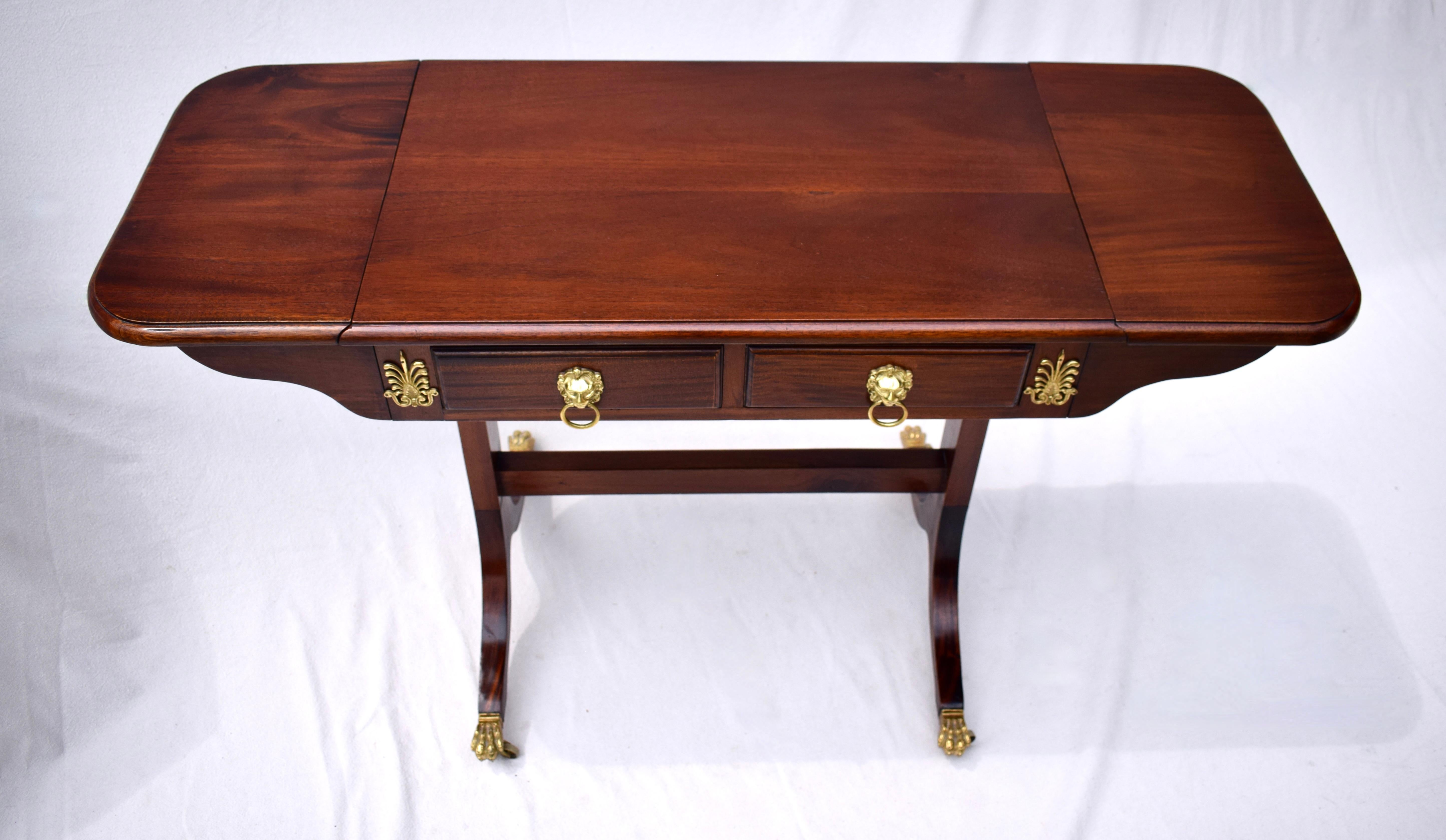 English Georgian style Mahogany drop-leaf console, desk or work table with two fitted dovetail drawers, embellished with brass ornamentation & lions head pulls. The supporting & connecting stretcher terminates on splayed legs with lion paw brass
