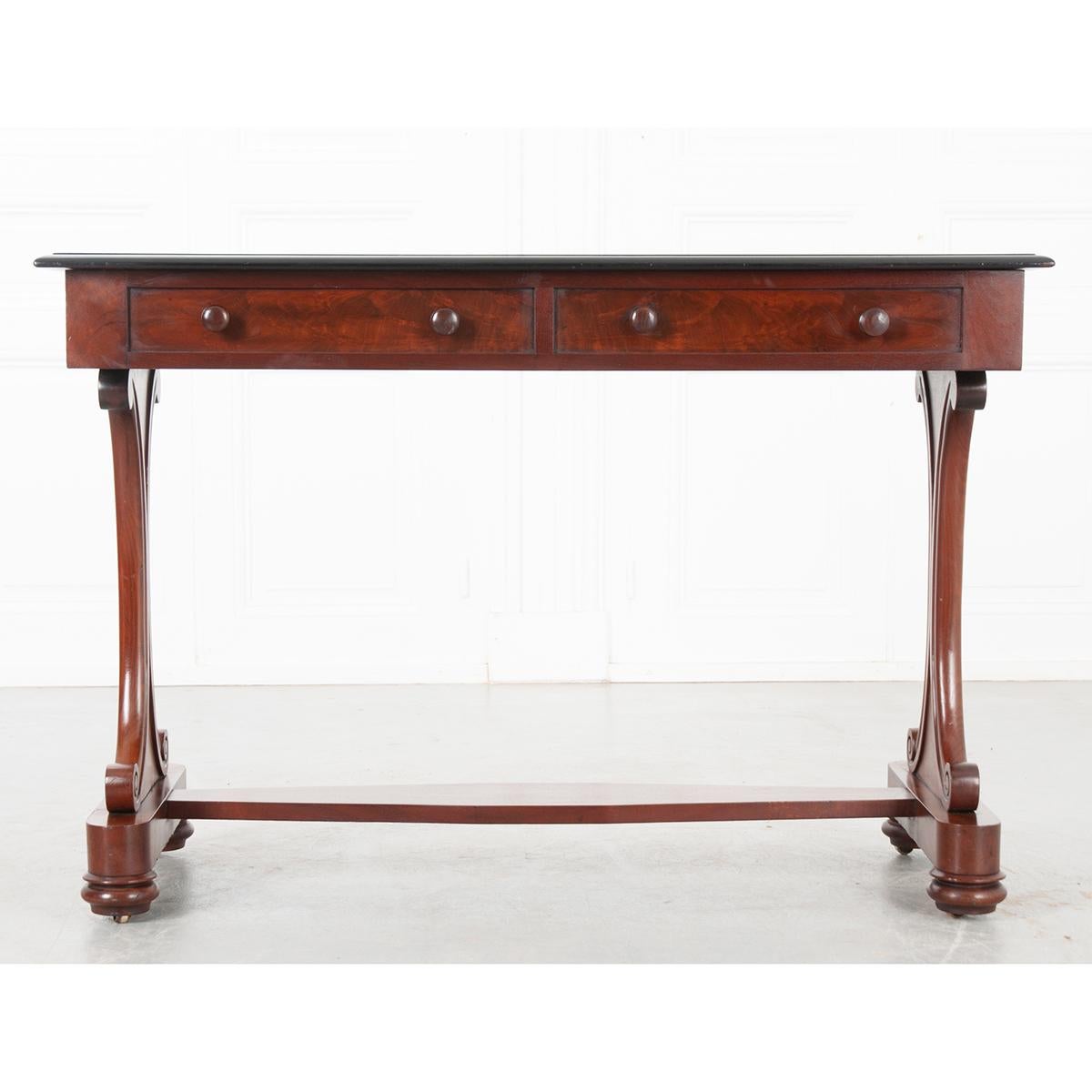 This is an English pedestal desk with two faux drawers just under the ebonized top. All sit on a curved pedestal atop a plinth base with bun feet on top of metal casters. The base is connected by a flat stretcher. A pretty little table! Circa
