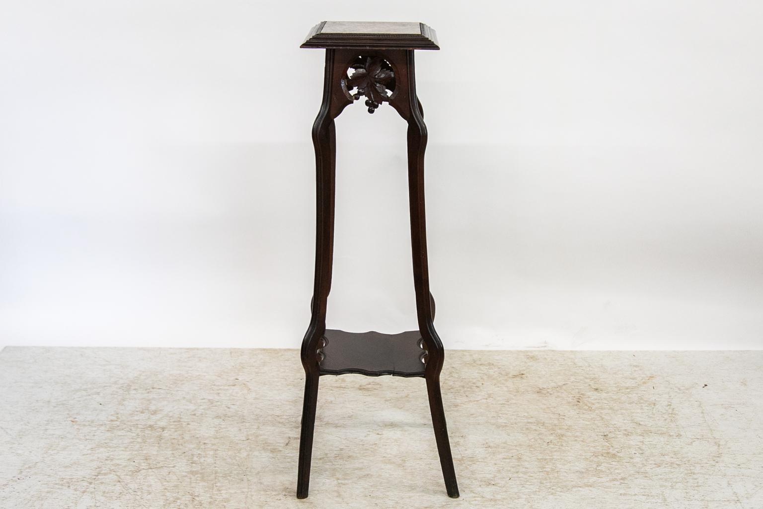 Ce pied de fougère présente un plateau fixe en marbre encadré de moulures en forme d'oves et de fléchettes, avec un tablier supérieur sculpté de raisins et de vignes. Les pieds sont doublement serpentins et sont soutenus par une tablette en placage