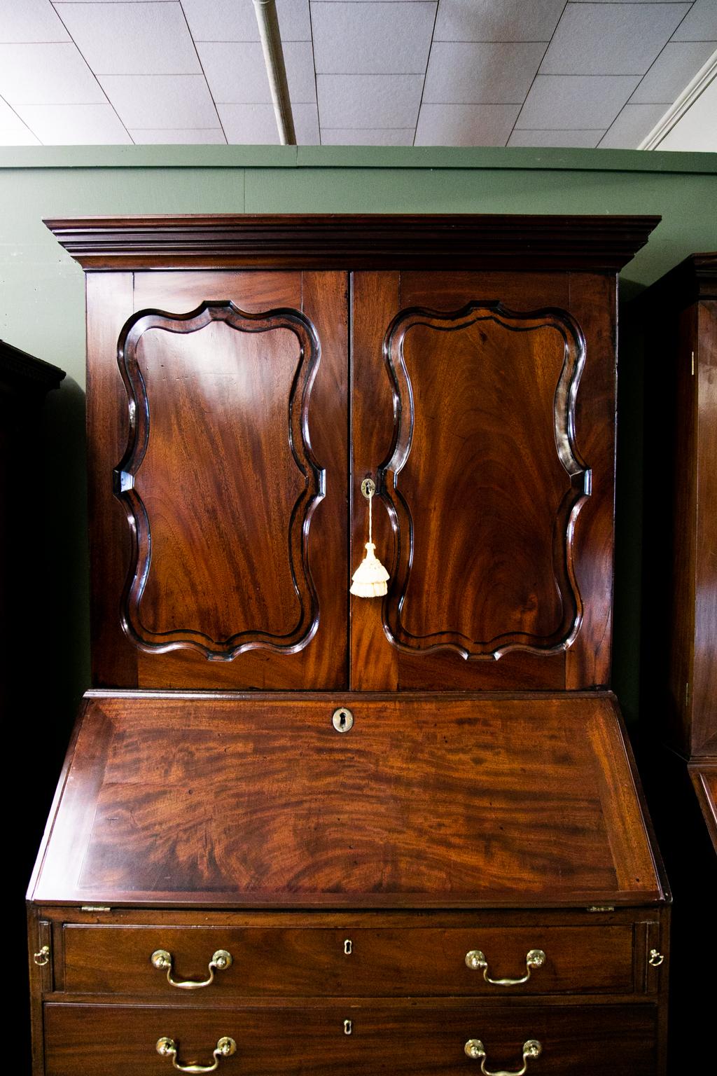 English Mahogany George II secretary, has raised serpentine panels. The interior features a prospect door with a geometric inlaid star of ebony and satinwood, and there are eleven drawers and cubby holes.
