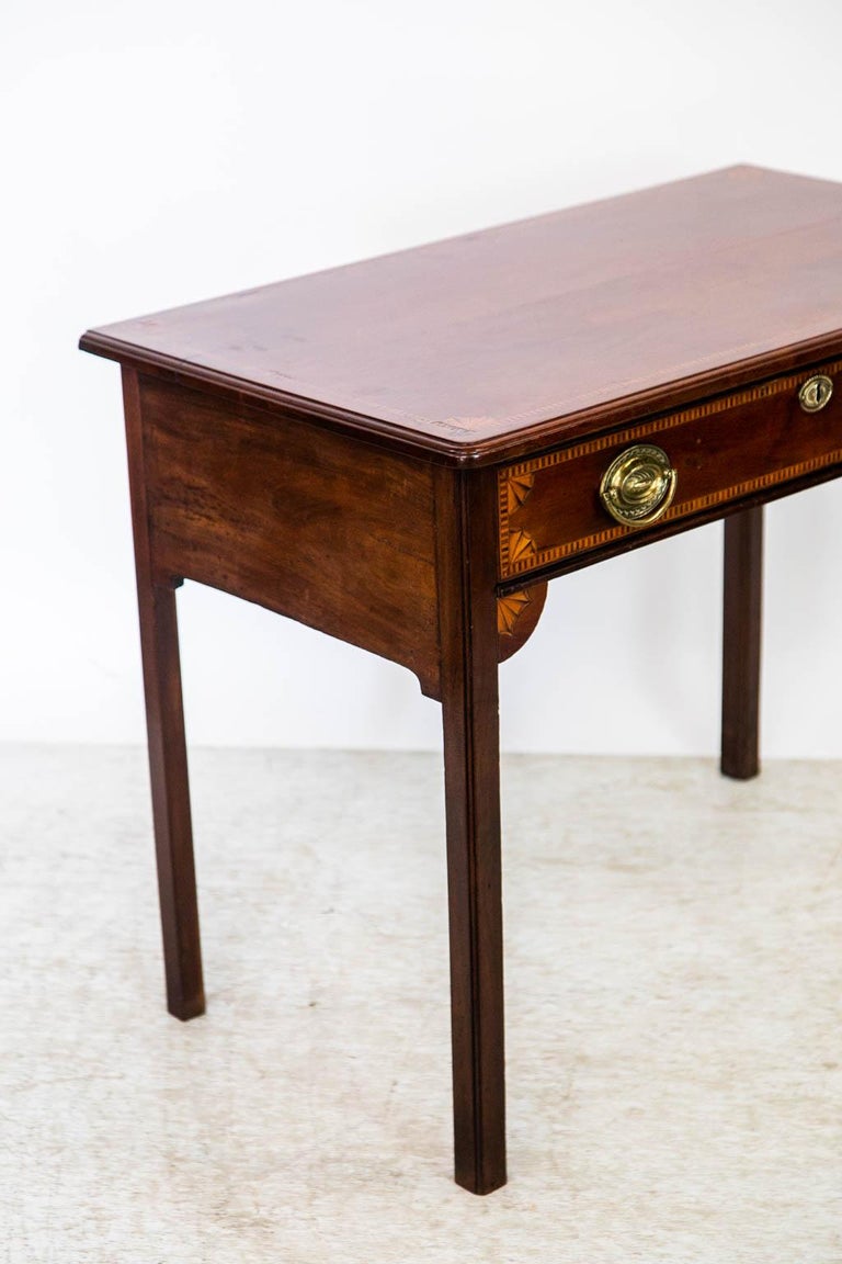 The top of this side table has a molded edge and has inlay banding comprised of ebony, rosewood, and satinwood in a repeating rectangle pattern. There are four quarter fans inside the top banding and the drawer front. Below the drawer there is