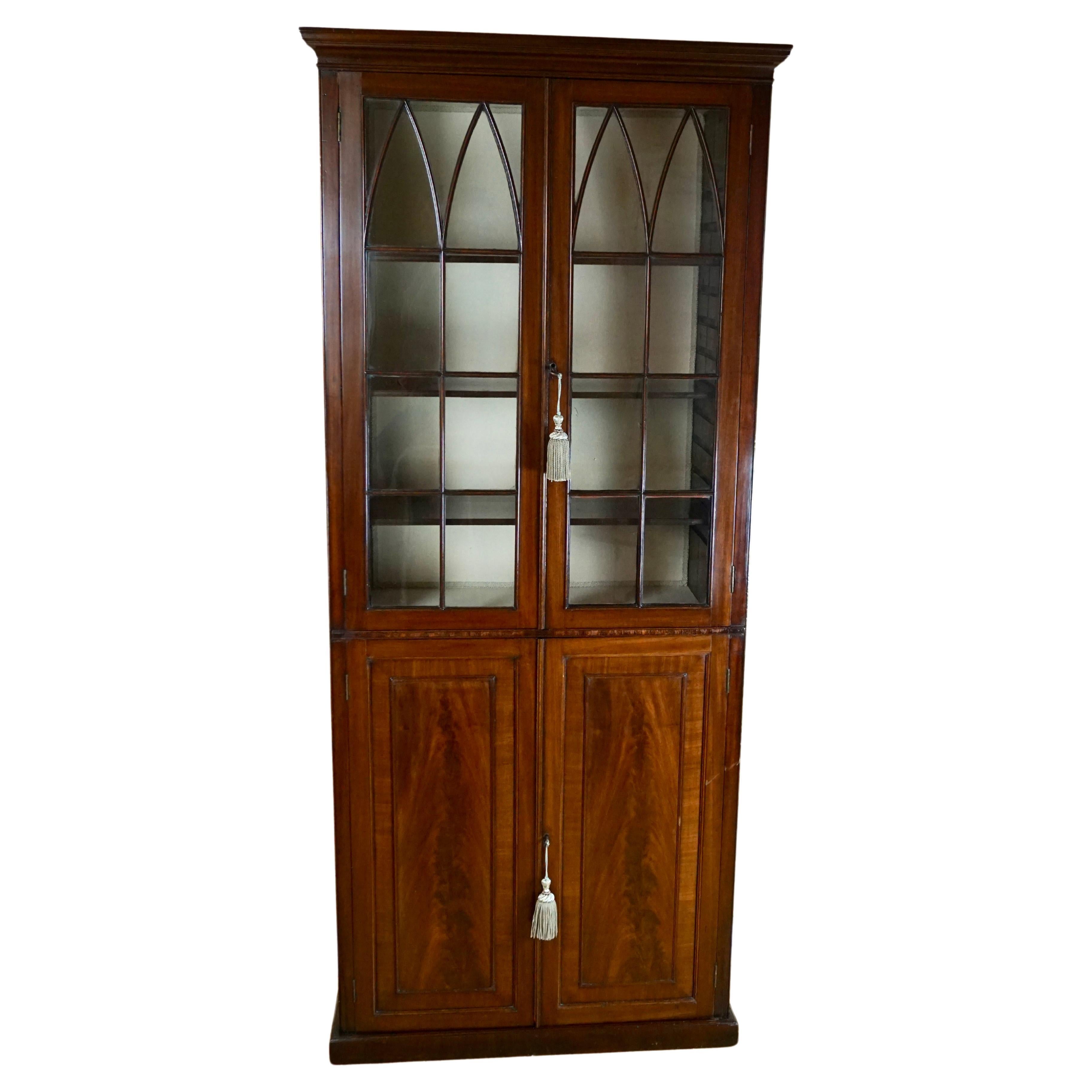 An English mahogany one piece bookcase, the molded crown above double astragal glazed doors with adjustable shelves over a pair of crotch mahogany panelled doors. The whole rests on a plinth base. Circa 1770-1800. Restored.