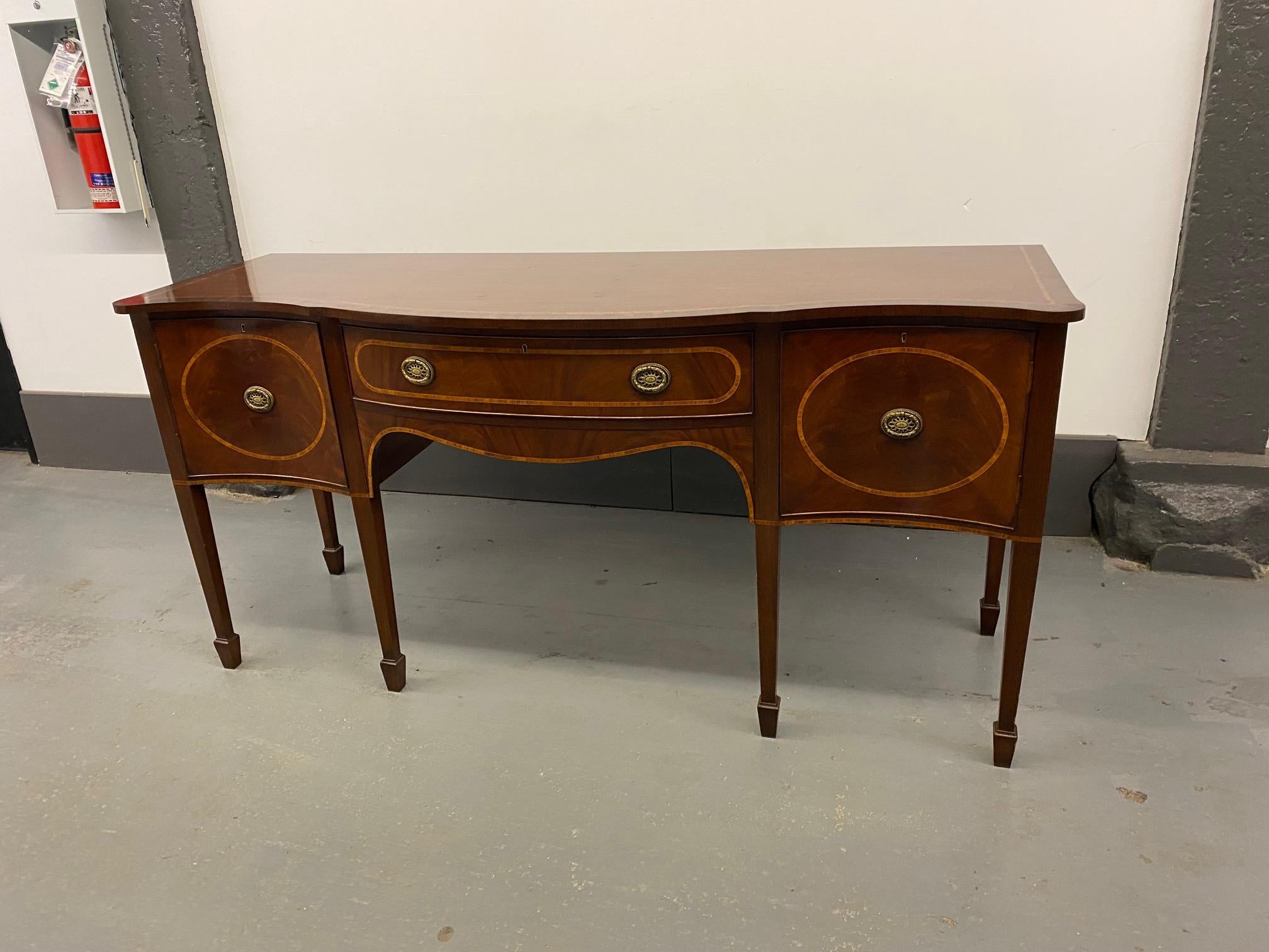 English Georgian style serpentine front figured mahogany side board, inlaid with boxwood cross-banding, fitted with cast brass pulls.