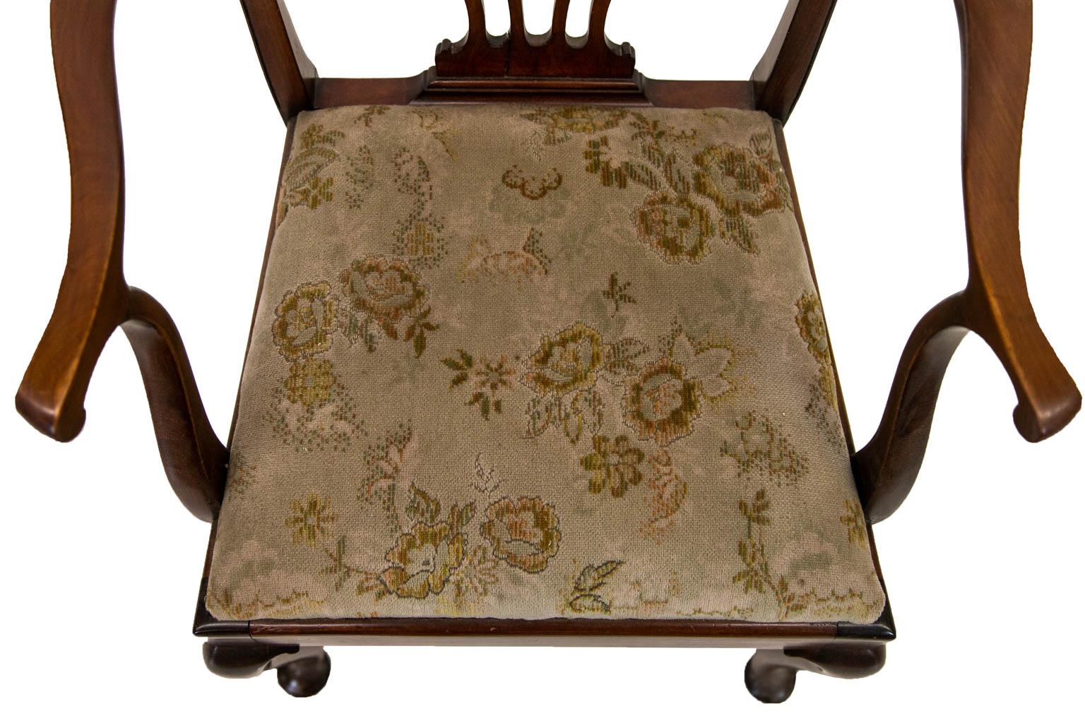 The back splat of this armchair is carved with pierced stylized Gothic arches. The crest rail has incised beading and two carved volutes. There are two shepherd's crook arms. The legs terminate in pad feet. The seat is removable. The upholstery has
