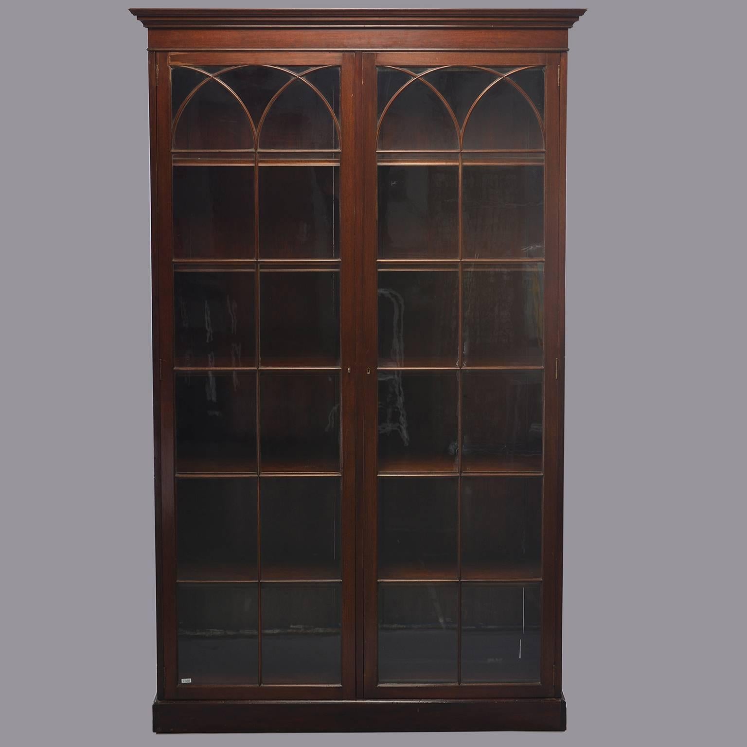 Tall English library cabinet is made of mahogany with decorative pediment, two glass front doors with working skeleton key locks and decorative arched trim, circa 1920s. Five internal fixed shelves.