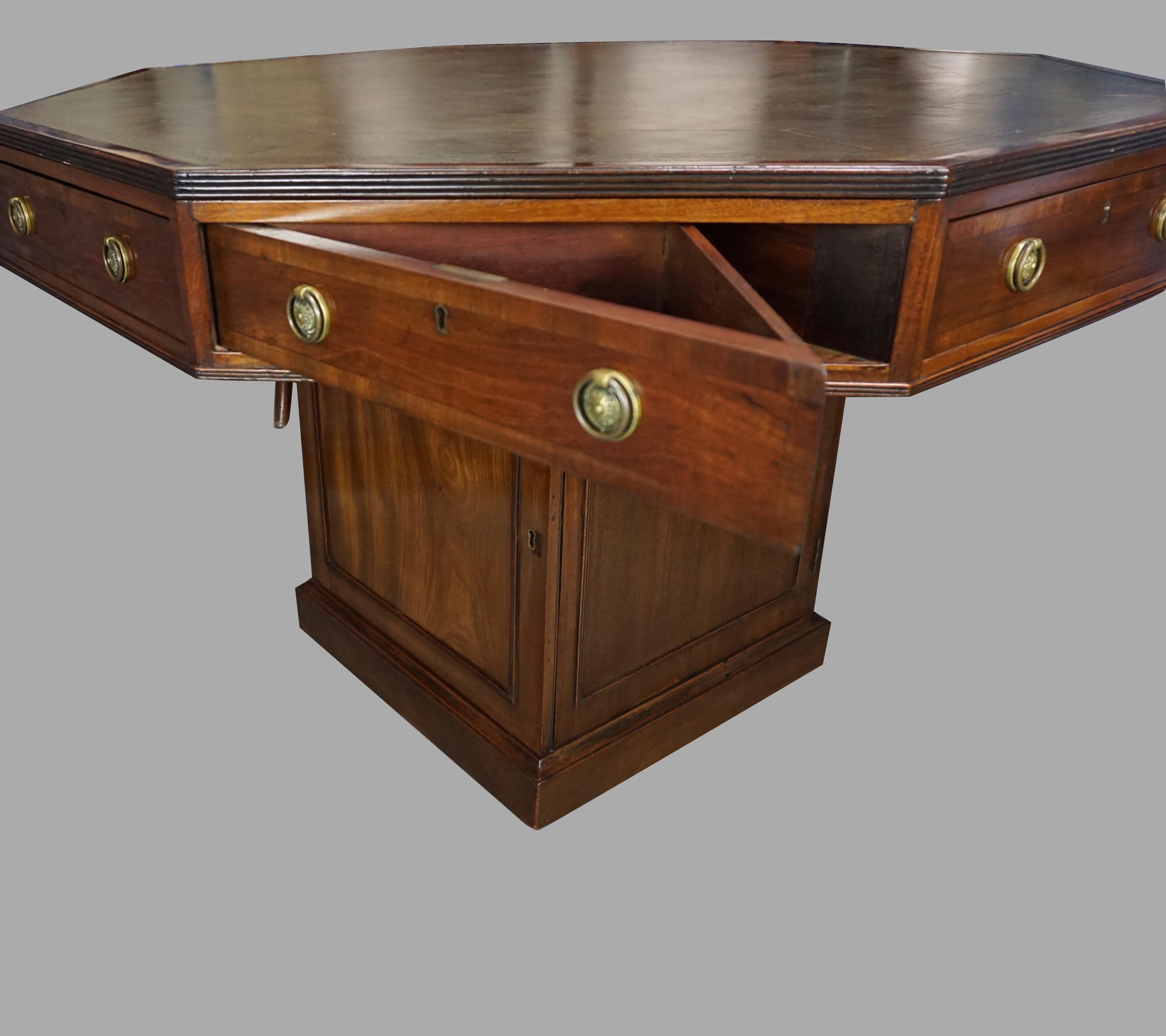 A fine quality English Georgian style drum or rent table, the gilt-tooled green leather covered octagonal top above 8 functional drawers, 4 pie shaped and 4 rectangular, supported on a square base with 2 opposing functional cupboard doors, on