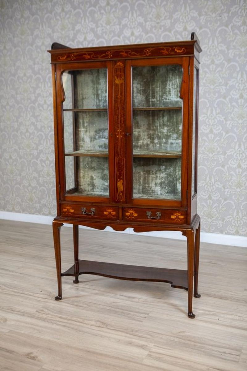 English Inlaid Mahogany Display Cabinet From the 19th Century

Step into timeless elegance with this exquisite antique display cabinet, a captivating example of early 20th-century craftsmanship. Standing gracefully on slender, cabriole legs with pad