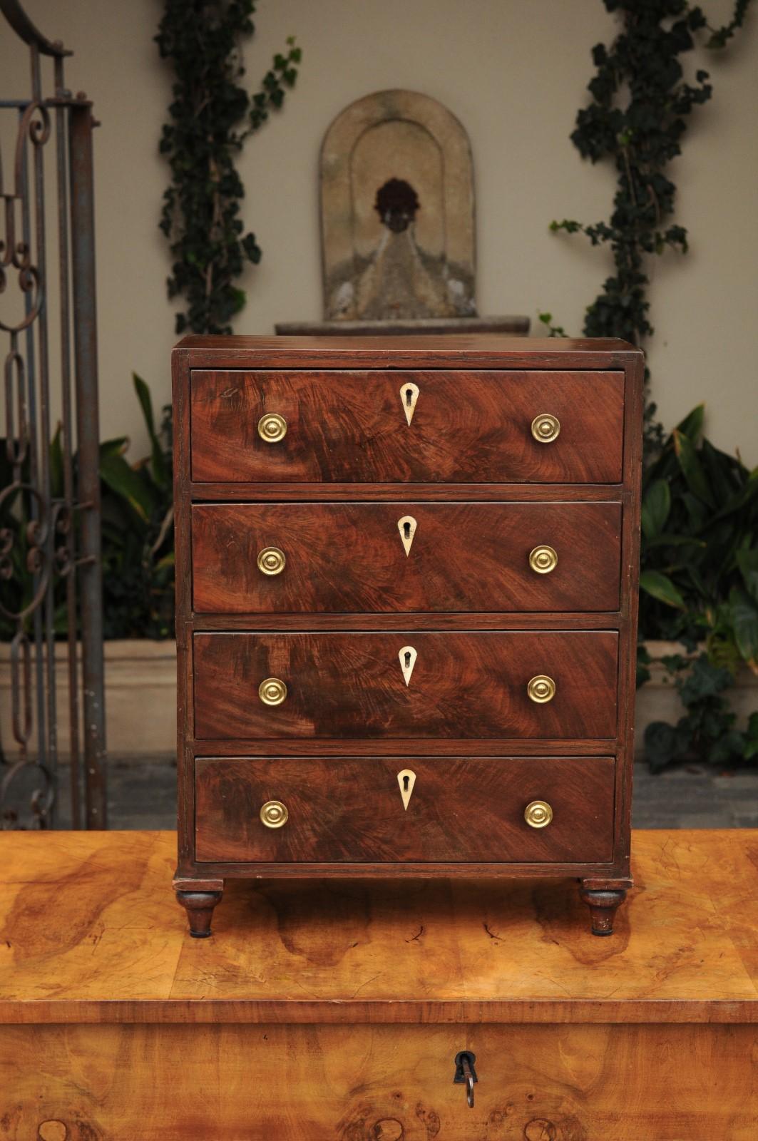 An English mahogany mini sample chest from the mid-19th century, with four drawers and toupie feet. Born in the middle of the 19th century, this petite English mahogany chest features a linear silhouette, whose apparent simplicity is perfectly