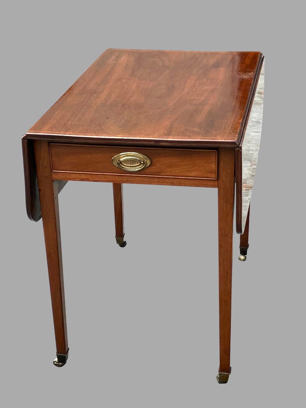 A rectangular English mahogany pembroke table of typical form, the top with a finely inlaid border above a central drawer, with 2 drop leaf sides, supported on square tapered legs ending in casters. French polished finish. Circa 1790.