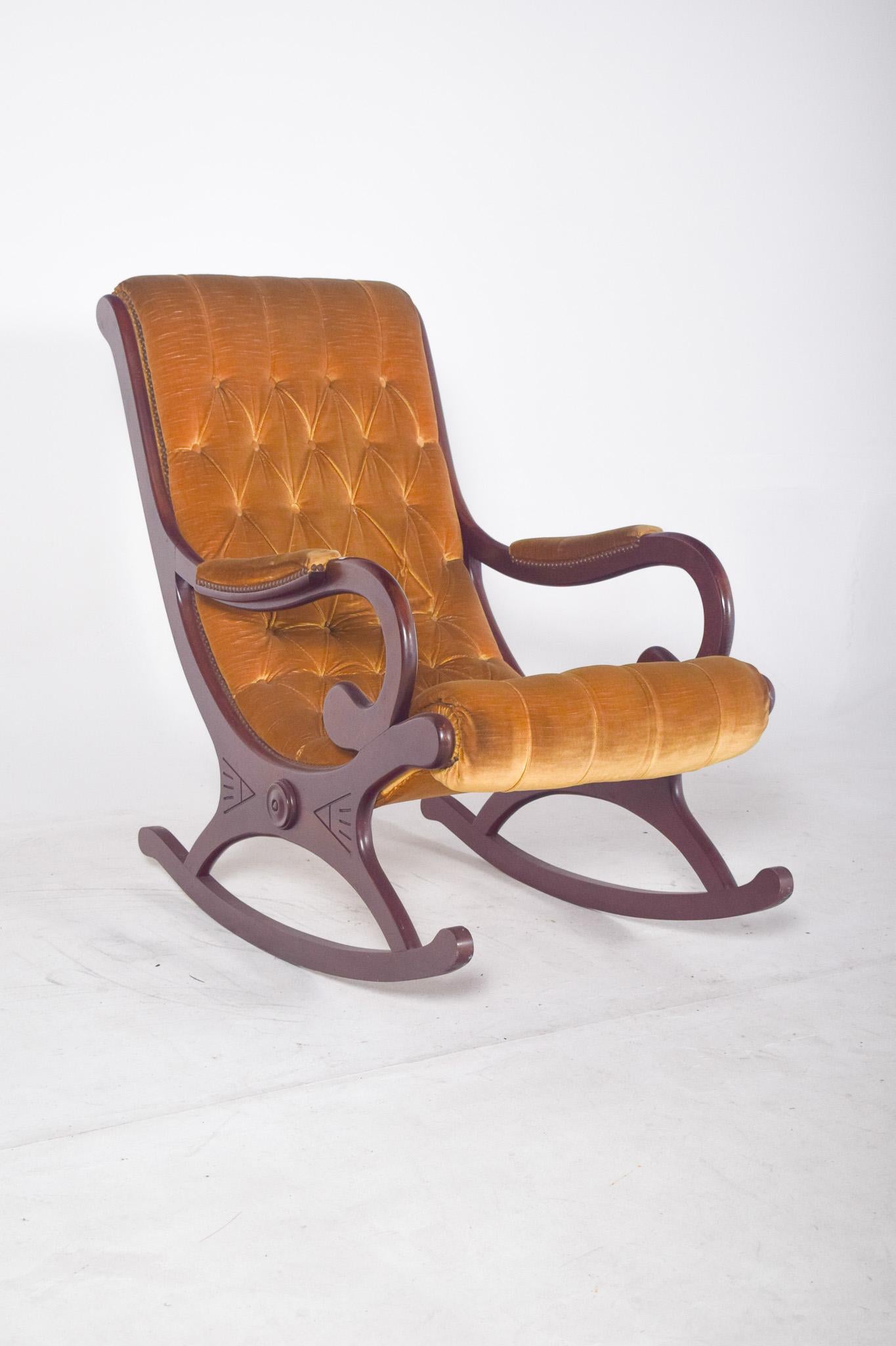 Sedia a dondolo rivestita in capitoné. Con un design elegante, la struttura è realizzata in legno massiccio scuro, con una finitura liscia e forme curve ben definite che integrano i braccioli e i piedi a dondolo in un unico flusso. La seduta e lo