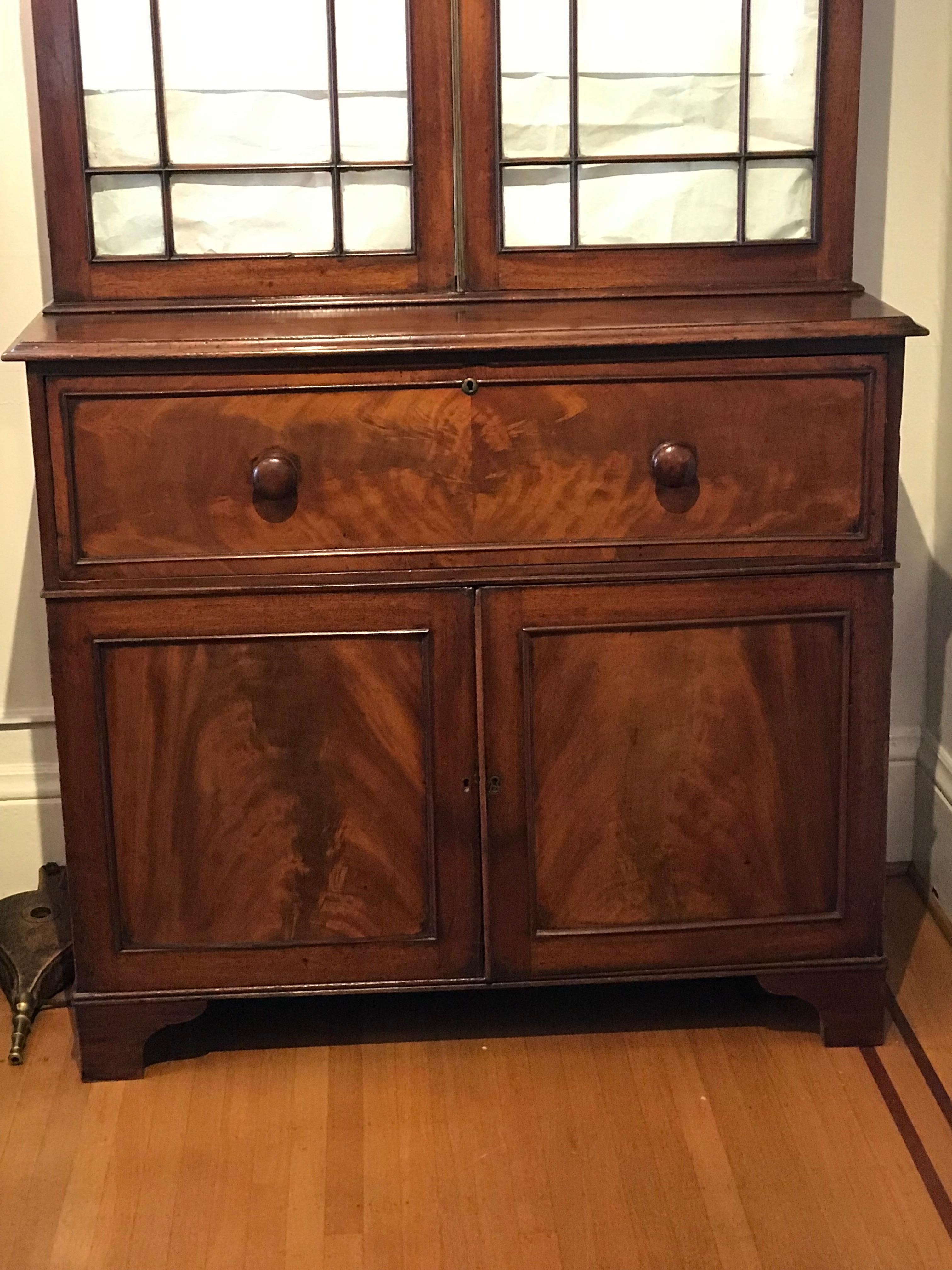 Secretary bookcase on desk. Drawer pulls out and front drops down to reveal fitted desk interior. Lower two-door cabinet with one large drawer and shelves. Upper section with three wood shelves and glazed doors.

English mahogany. 19th century,