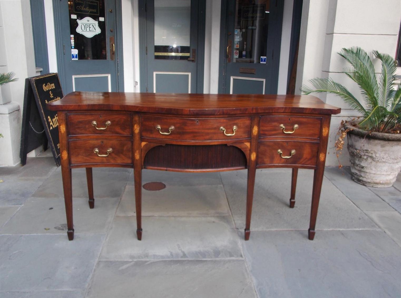 English mahogany serpentine sideboard with a centered drawer over two sliding tambour doors, flanking end drawers, original brasses, oval satinwood patera inlays, and terminating on tapered legs with spade feet, Late 18th century.