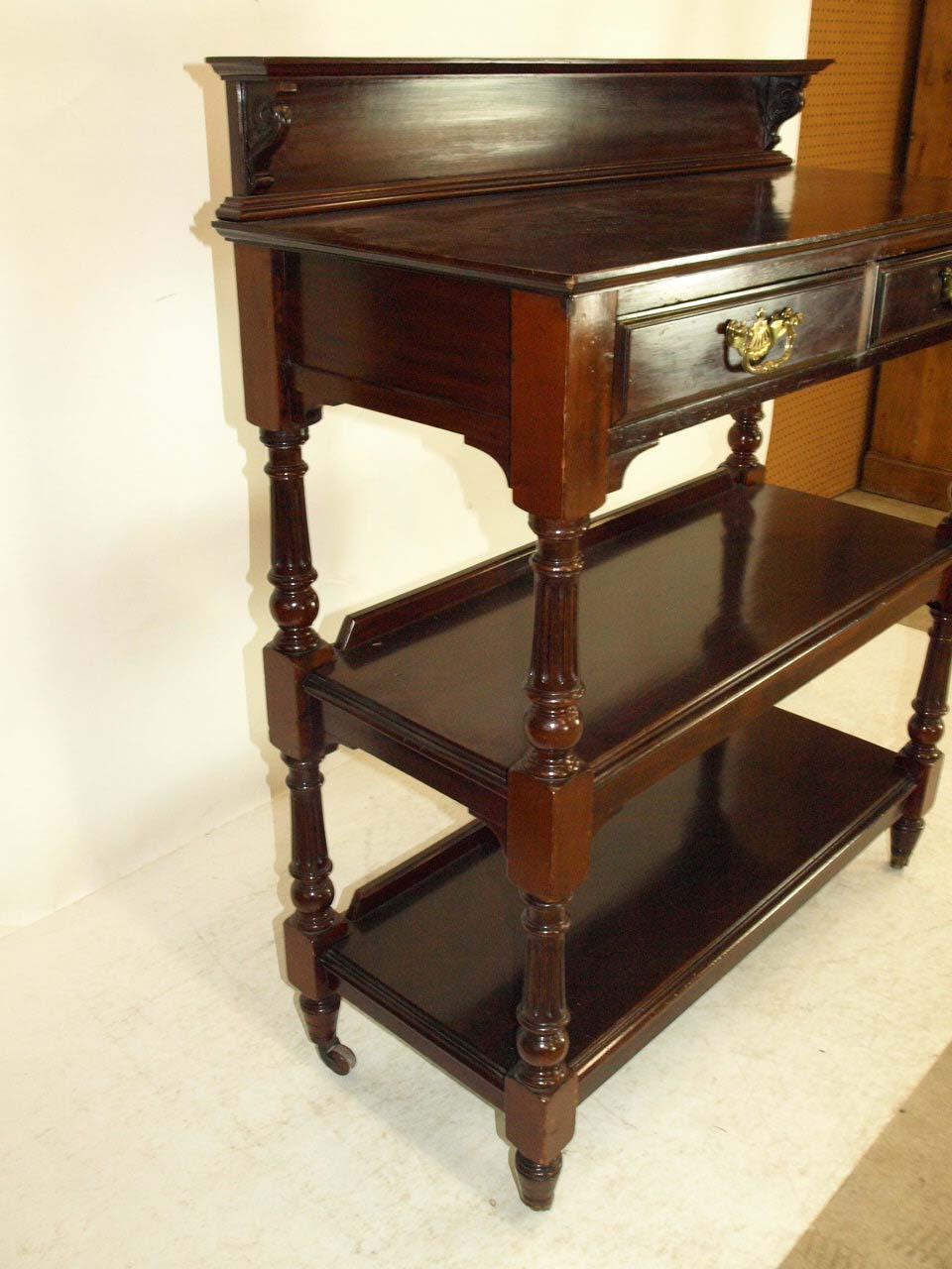 English mahogany serving trolley, the gallery with carved supports, two drawers with original brass pulls, two lower shelves, resting on brass and brown porcelain castors, circa 1890.