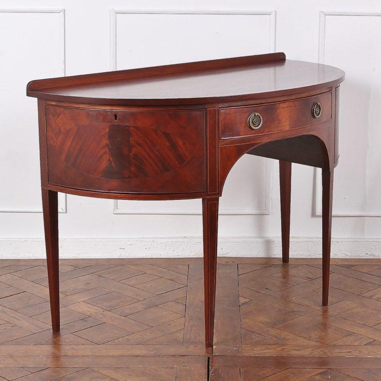 An English, inlaid mahogany, Sheraton Revival demilune serving table or console, having a centre drawer flanked by two small cabinets, all featuring flame mahogany veneer and inlay. Solid mahogany top with banded edge.
