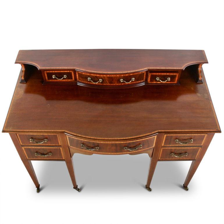 An English Sheraton-Revival server in solid mahogany, the nine drawers cross-banded in satinwood and with further satinwood banding to the edges of the surface. The piece stands on square tapering legs terminating in brass castors. An Edwardian-era