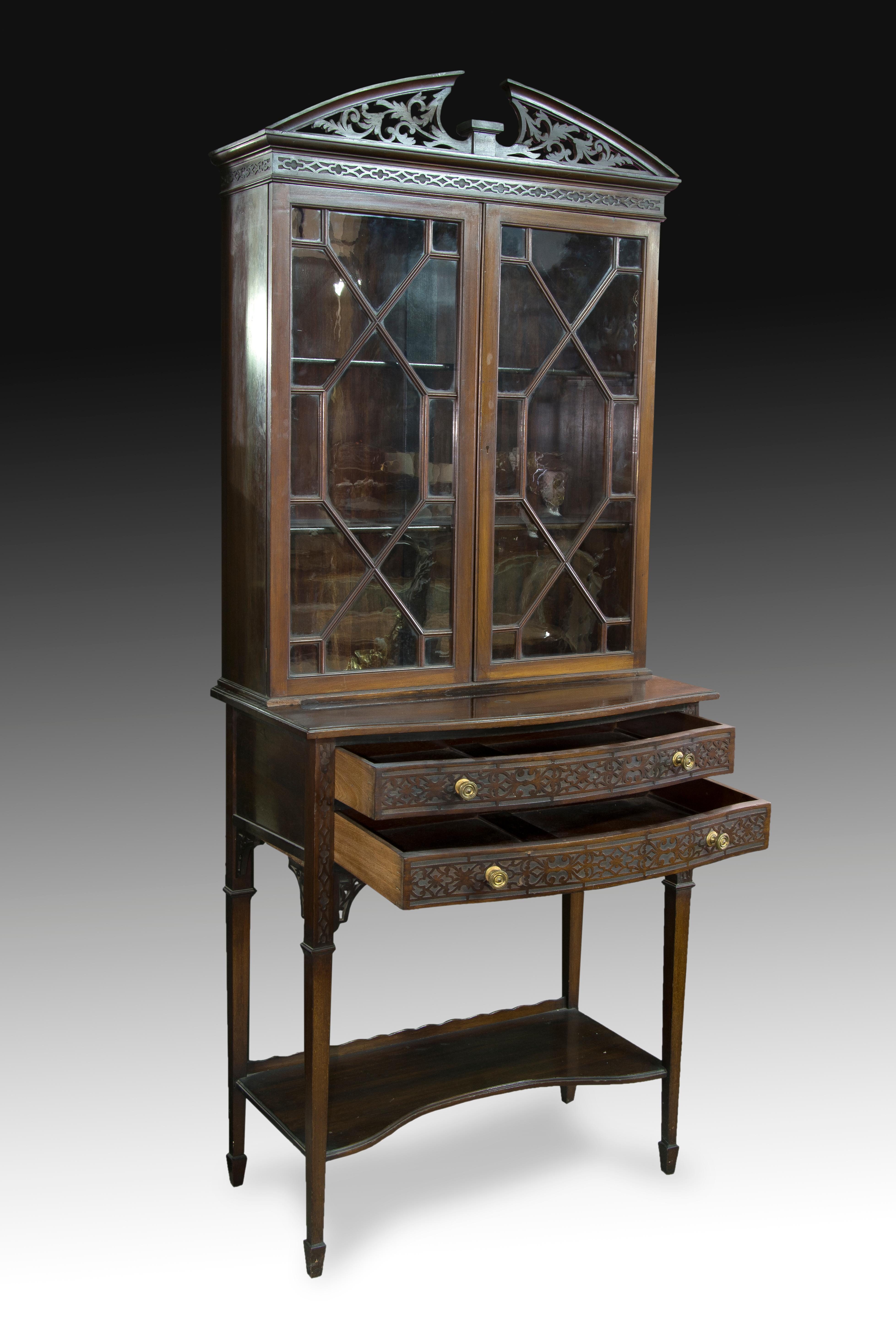 English showcase. Mahogany wood, XIX century. 
 Showcase with shelves and two doors with glass and geometric decoration topped by a split pediment with vegetal decoration, which is presented on a cabinet with two drawers in front, four legs and a