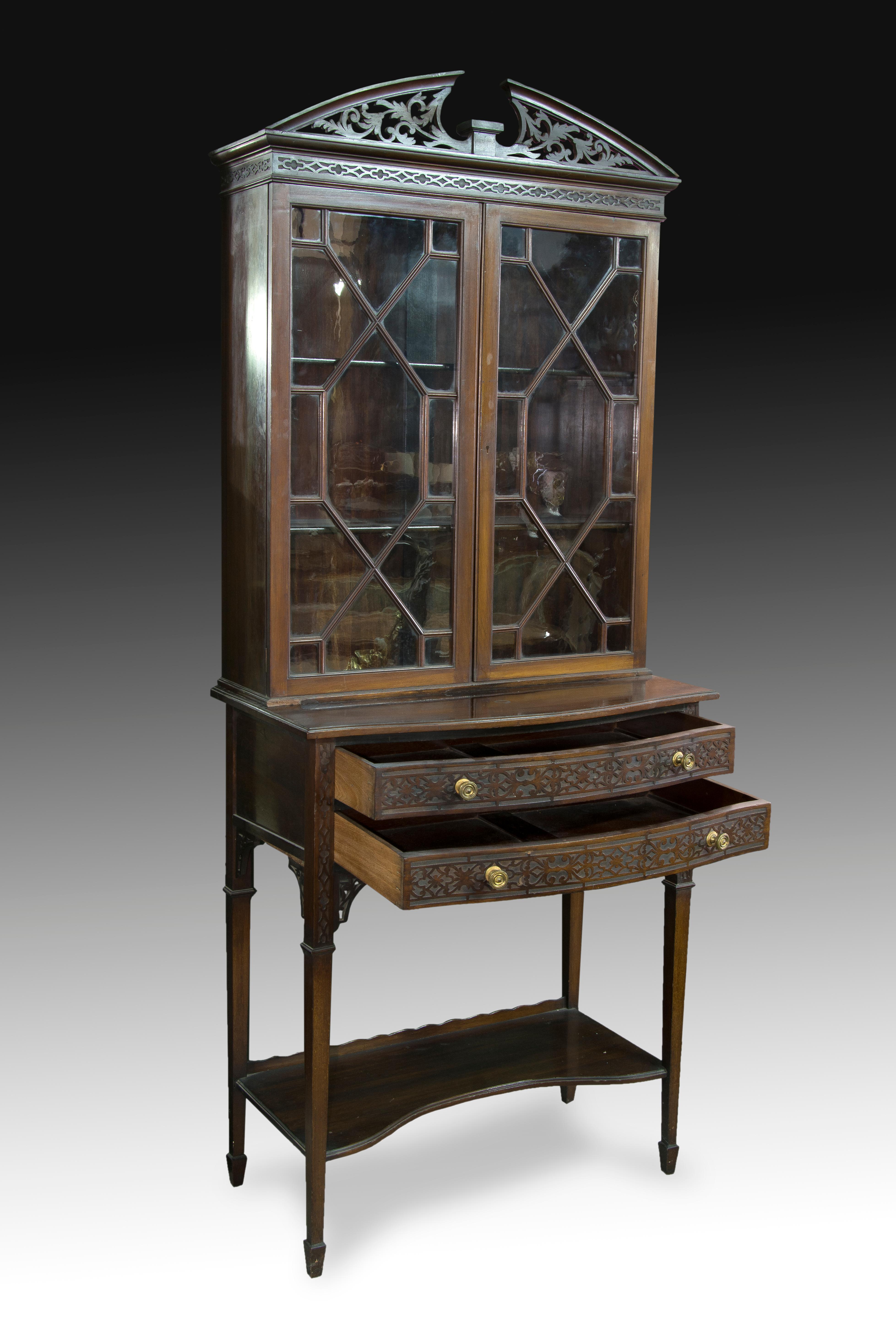 Englischer Schaukasten. Mahagoniholz, XIX Jahrhundert. 
 Vitrine mit Einlegeböden und zwei Türen mit Glas und geometrischem Dekor, gekrönt von einem geteilten Giebel mit pflanzlichem Dekor, der auf einem Schrank mit zwei Schubladen vorne, vier