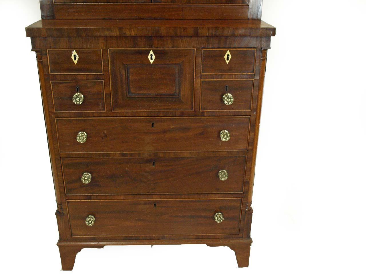 English mahogany step back press, the top with inset panels surrounded by cross banded mahogany, lower section with unusual drawer arrangement( small and deep drawers over three graduated drawers) , inset quarter column , brass knobs, resting on