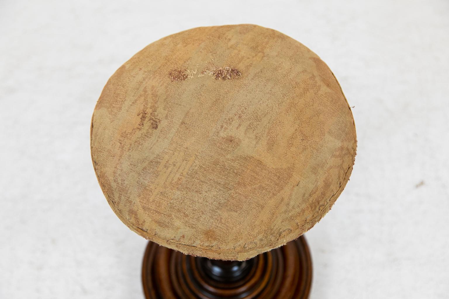 English mahogany stool, the stem has gun barrel turning on the base with concentric circle ogee molding. The upholstery is well worn.