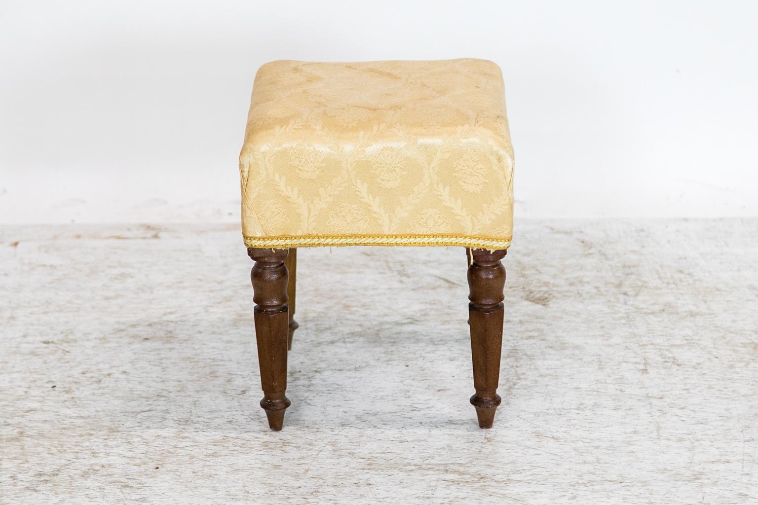 The legs of this stool are turned at the top and extend in a hexagonal shape. The upholstery has stains and would need to be replaced.
  