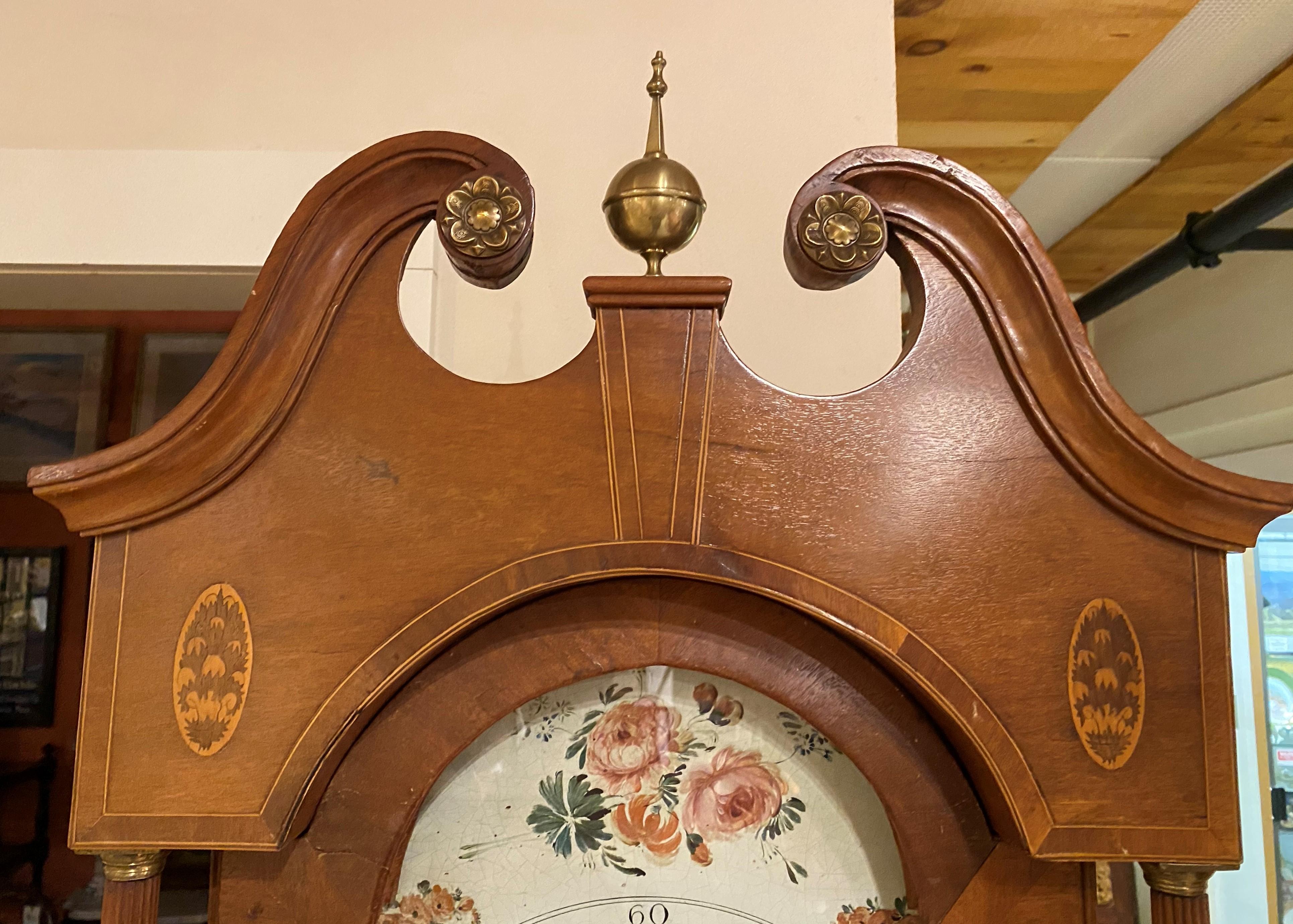 A fine English mahogany tall case clock or grandfather clock with broken arch bonnet highlighted with punched brass rosettes and central ball & spike finial, surmounting an arched glazed door, flanked by oval foliate paterae, opening to a hand