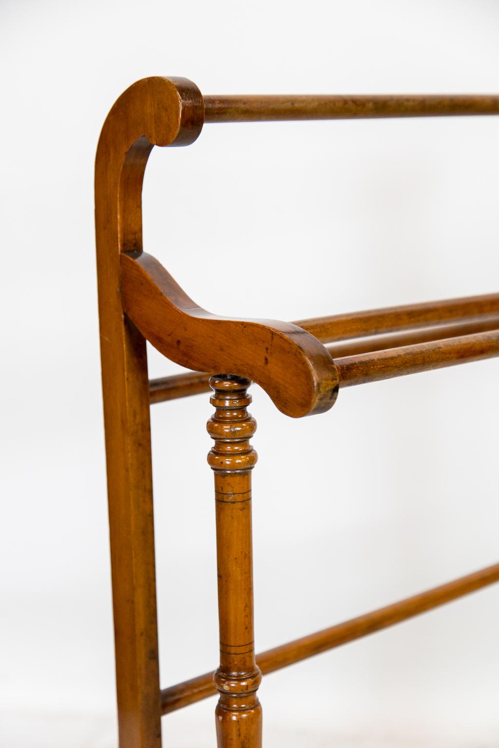 This rack has a rear leg with a scrolled upper top connected by a cross bar. The middle bars are supported by scrolled arms which are in turn supported by turned legs.