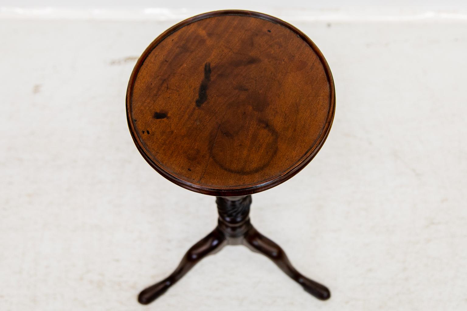 This table has a vase turned stem above a spiraled knop. Two of the legs have been reinforced at some time with a screw that has been filled over with a circular plug. The top has some dark stains and a minor shrinkage crack. The top has a shallow