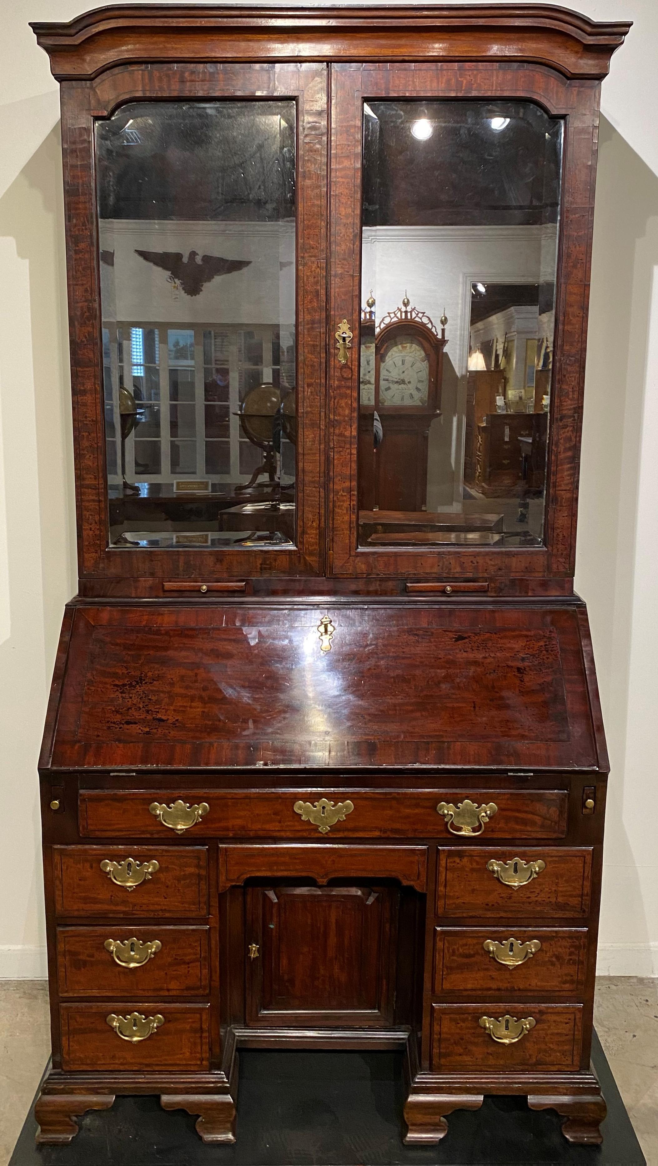 A spectacular English mahogany two part secretary, its upper case with shaped cornice surmounting two conforming beveled mirror doors, opening to an elaborate compartmentalized interior with a center prospect door, open shelves, valanced cubbies,
