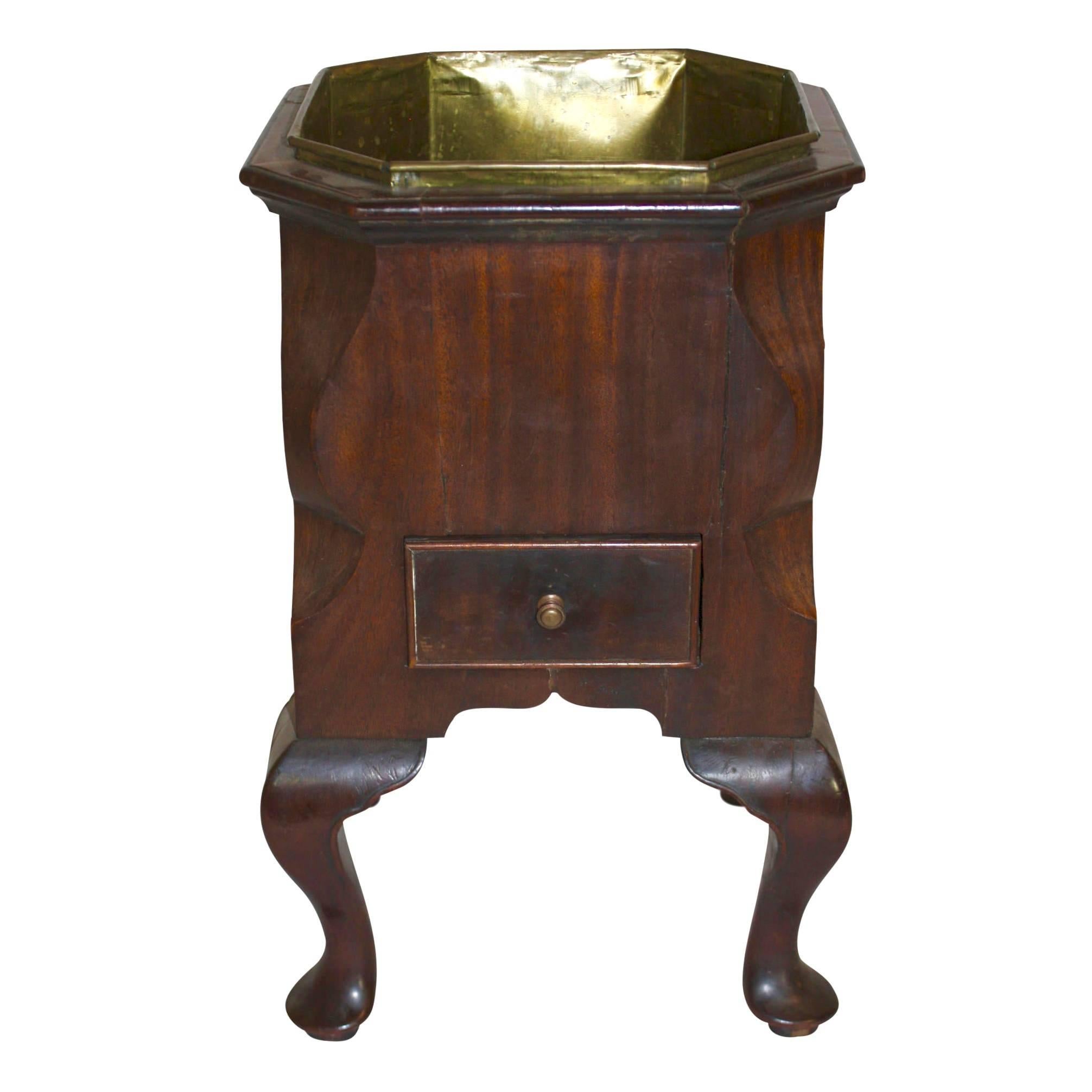 This open wine cooler is made of mahogany with a brass liner and brass handles. Canted corners give the top an octagonal shape. The cooler is raised on four cabriole legs with pad feet. A lower drawer, which is 10 inches deep, is useful for storing